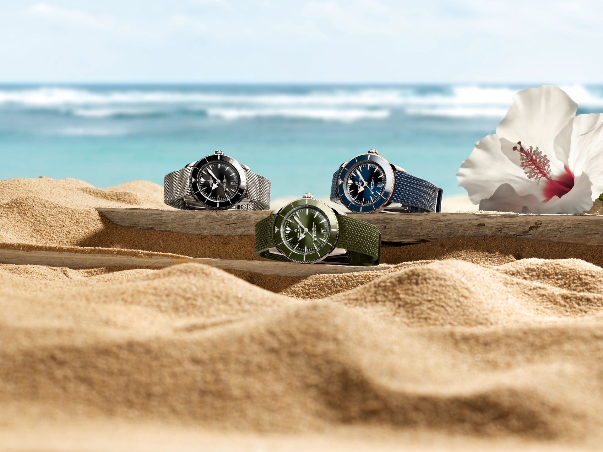Drie horloges op een zandstrand met de oceaan op de achtergrond en witte hibiscusbloemen.