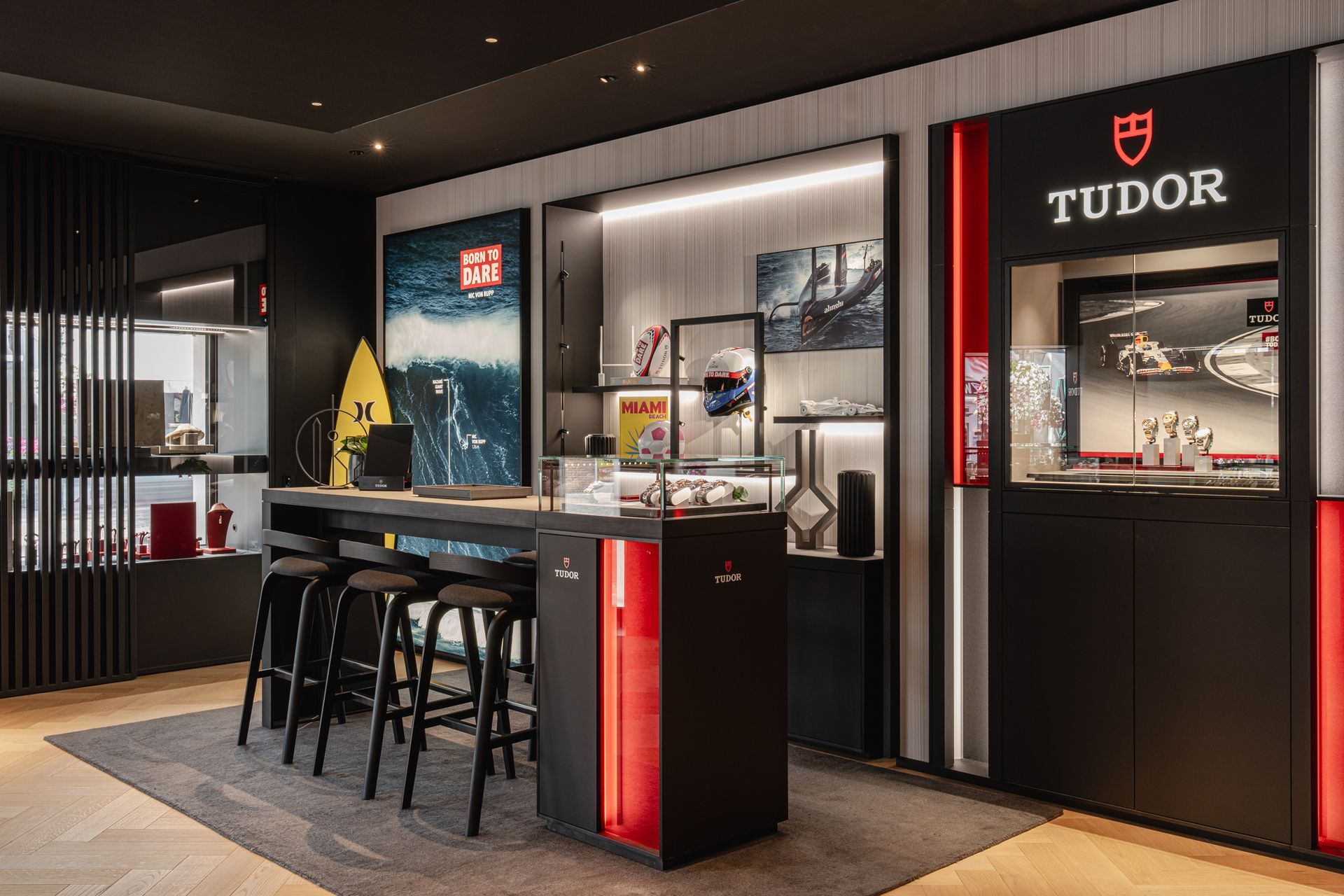 Een moderne Tudor-horlogewinkel met een zwart-rode bar, drie barkrukken en verlichte productvitrines.