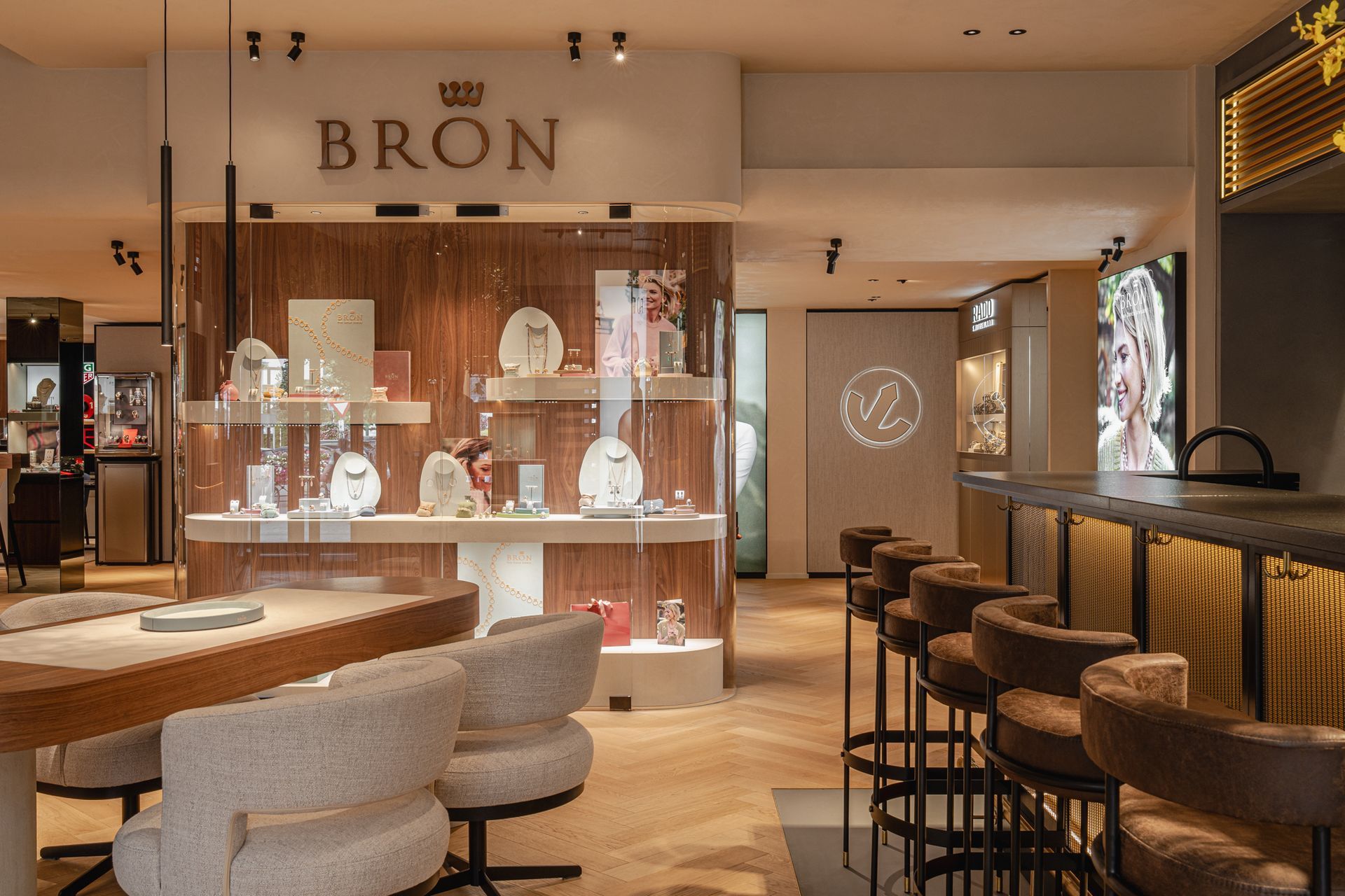 Interieur van een juwelierszaak met vitrines vol kettingen, een bar met barkrukken en een bord met de tekst