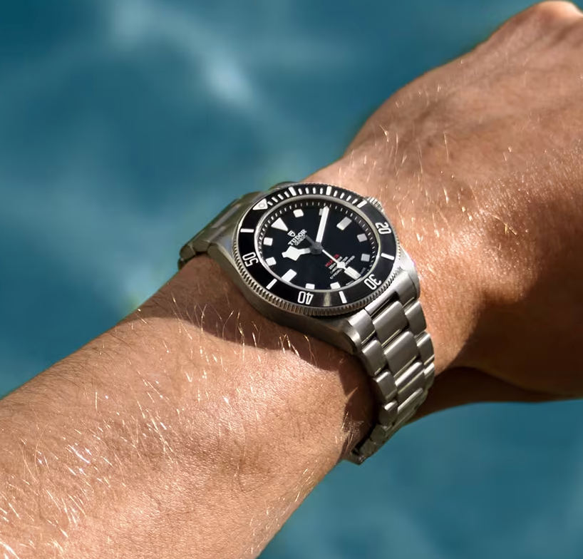 Close-up van een zilveren duikhorloge om een pols tegen een achtergrond van blauw water.