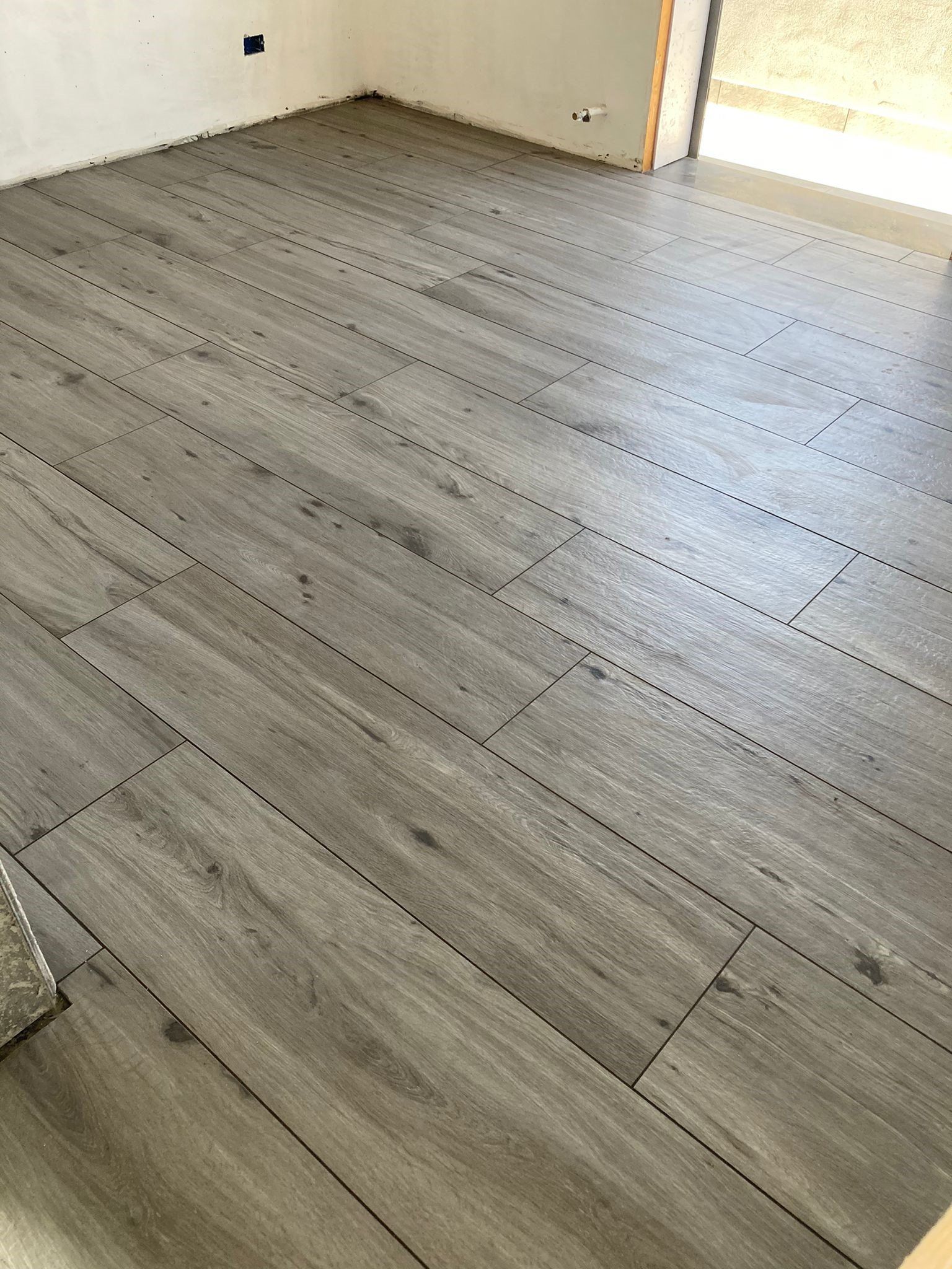 Una stanza con pavimento in legno e pavimento in piastrelle grigie.