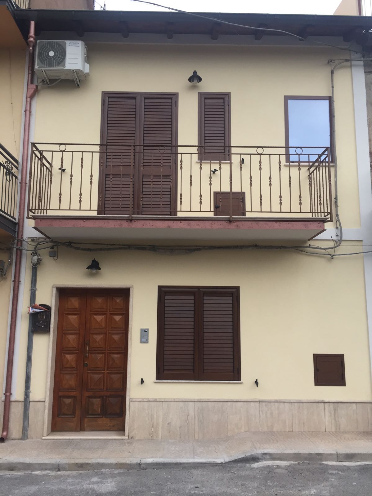 Una casa gialla con persiane marroni e un balcone