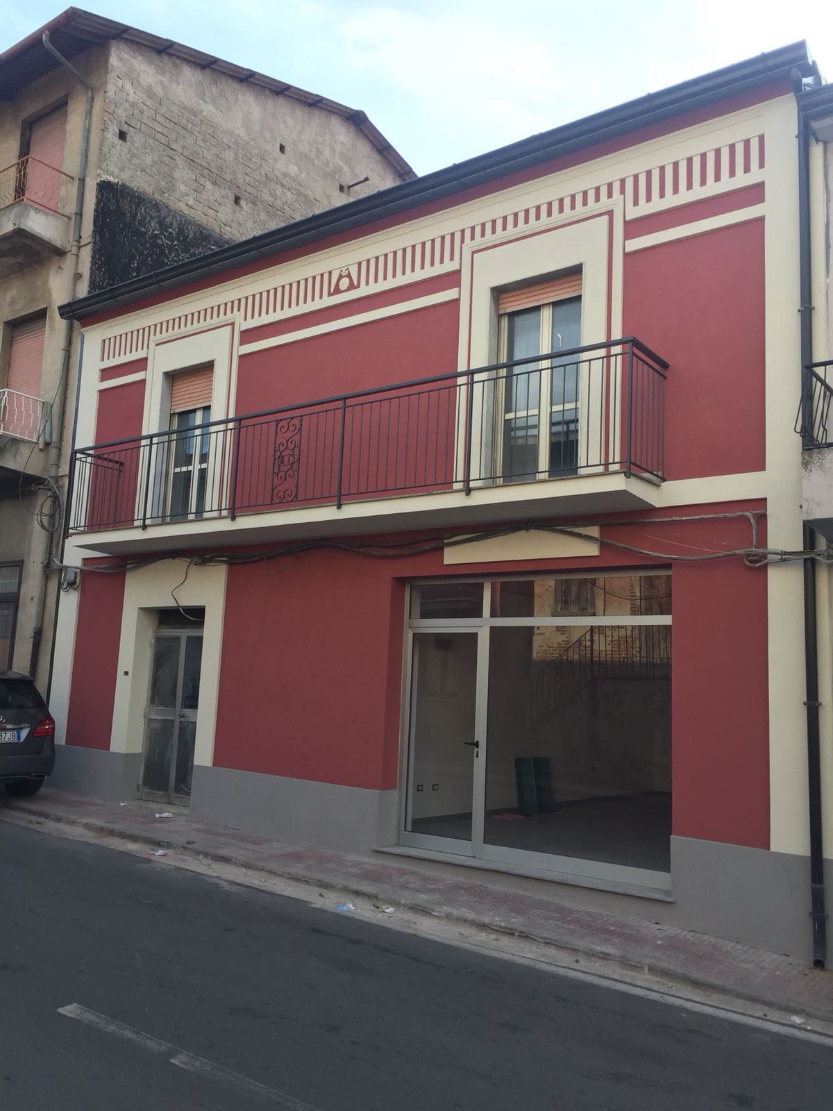 Un edificio rosso e bianco con un balcone e un'auto parcheggiata di fronte.