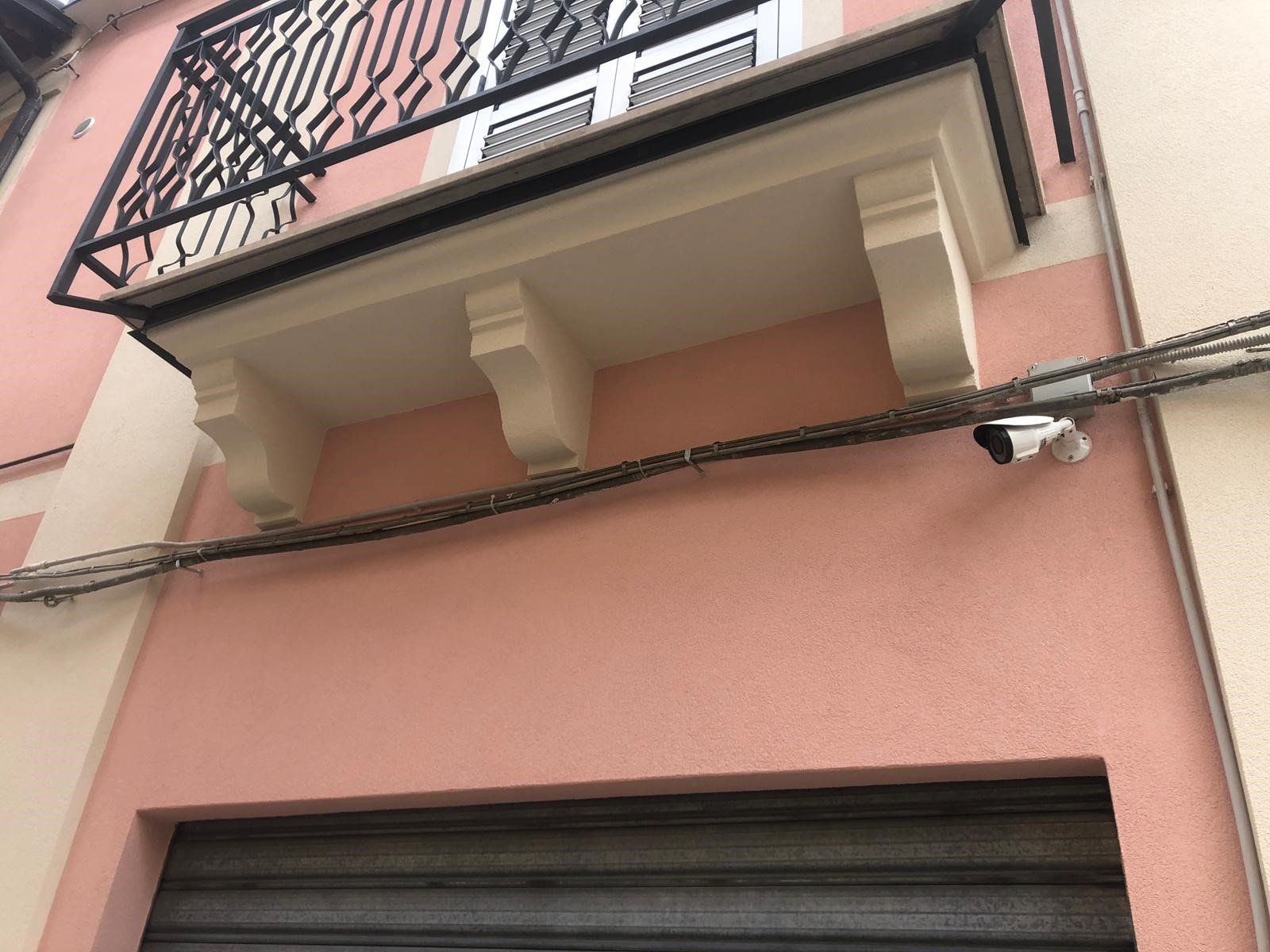 Un edificio rosa con un balcone e una telecamera sul lato
