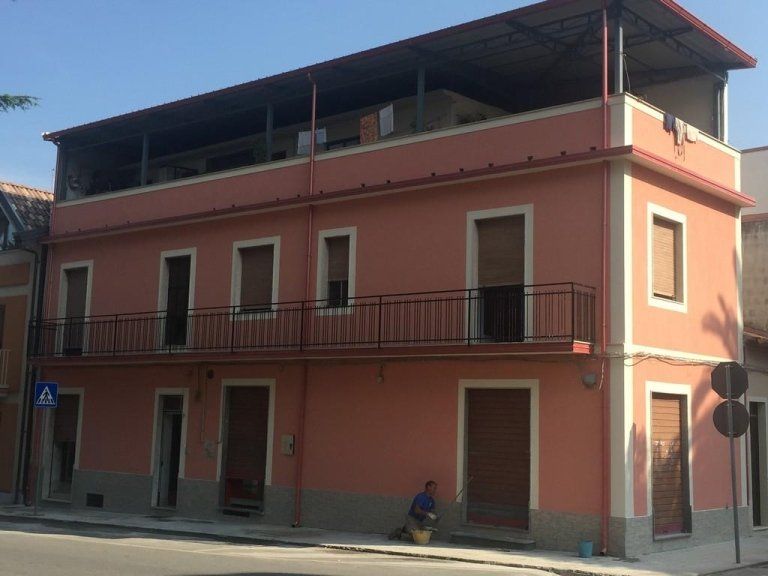 Un uomo è seduto sul marciapiede davanti a un edificio rosa