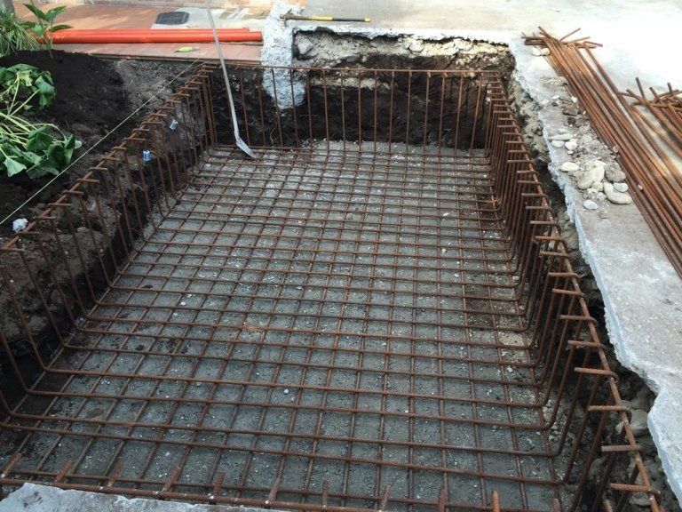 Un grande buco nel terreno viene riempito con cemento e barre d'acciaio.