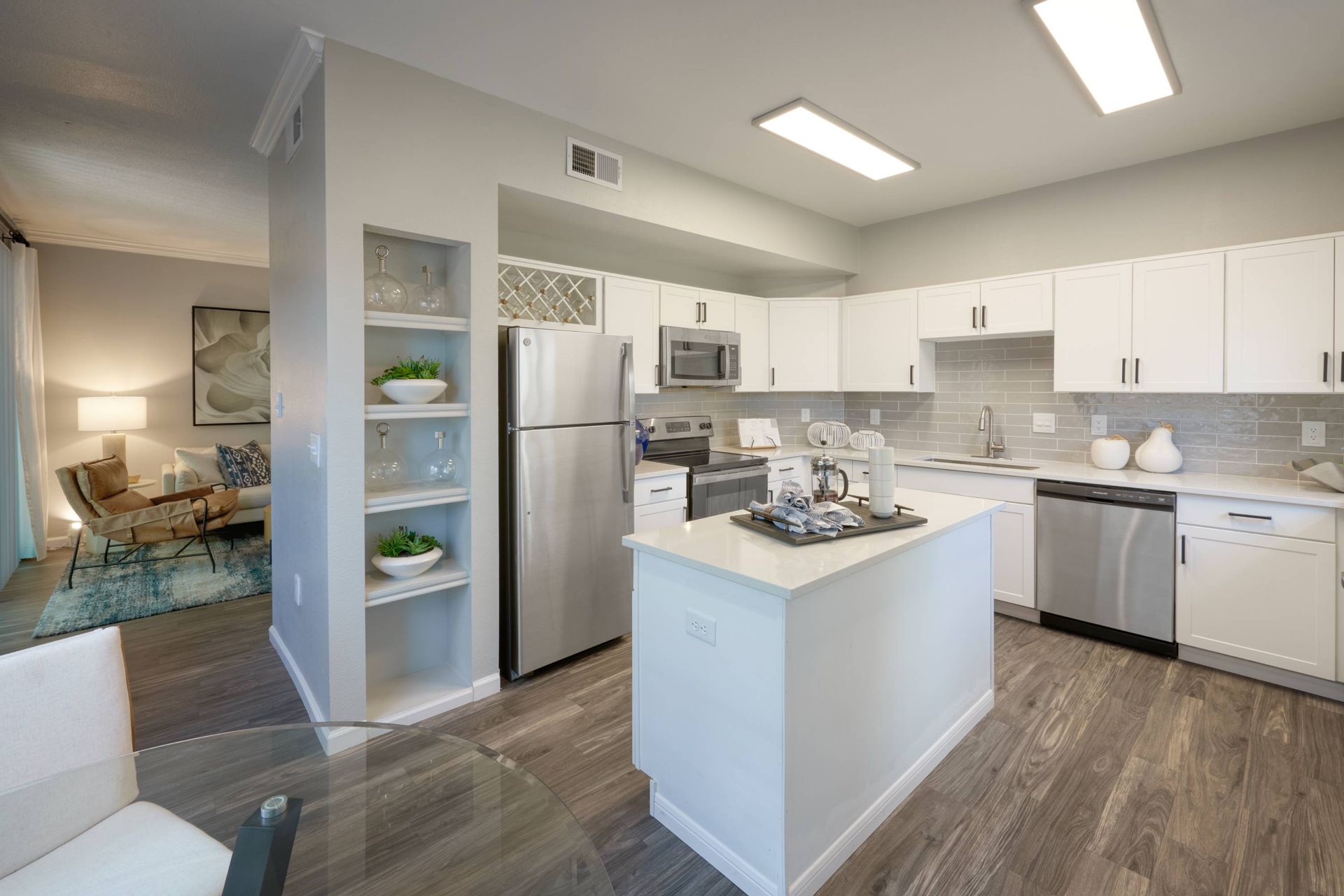 Open-concept kitchen with white cabinets, stainless steel appliances, island, and gray backsplash.