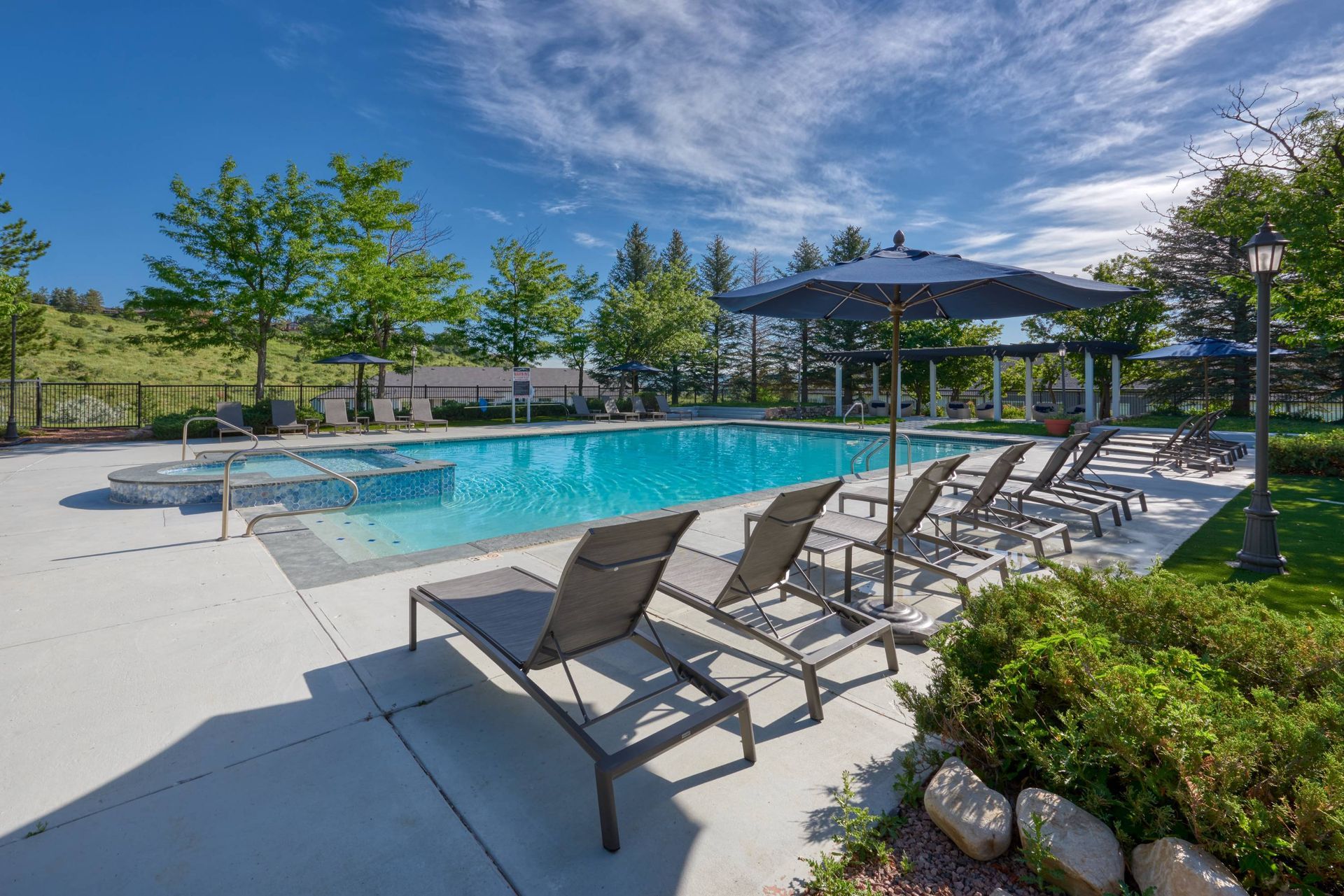 Outdoor apartment community pool with lounge chairs, umbrellas, and surrounding landscaping.