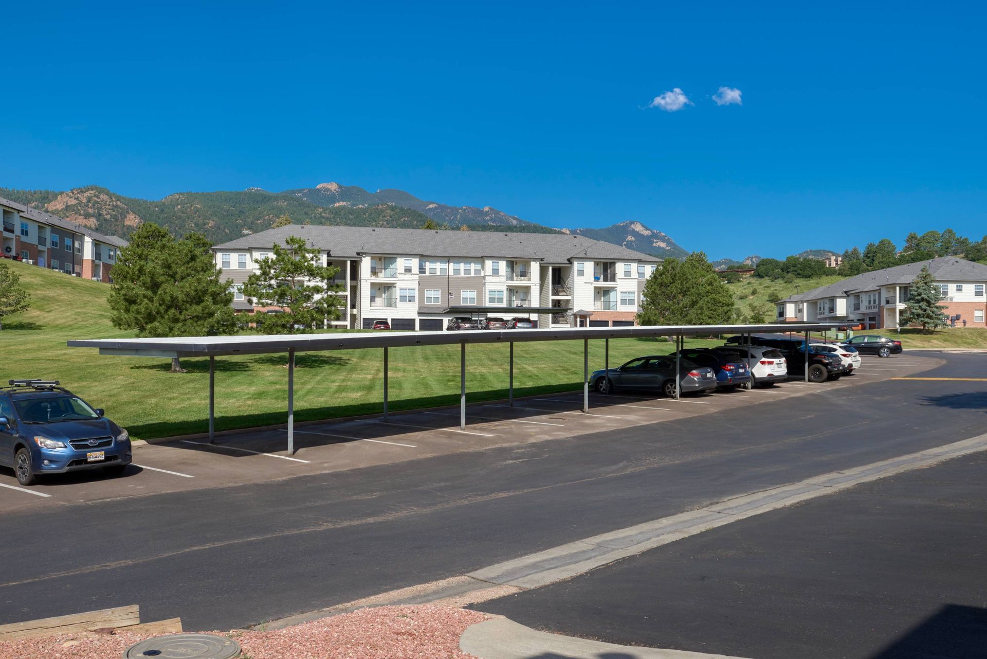 Exterior view of a multi-building apartment complex with a long covered parking area and mountain backdrop.