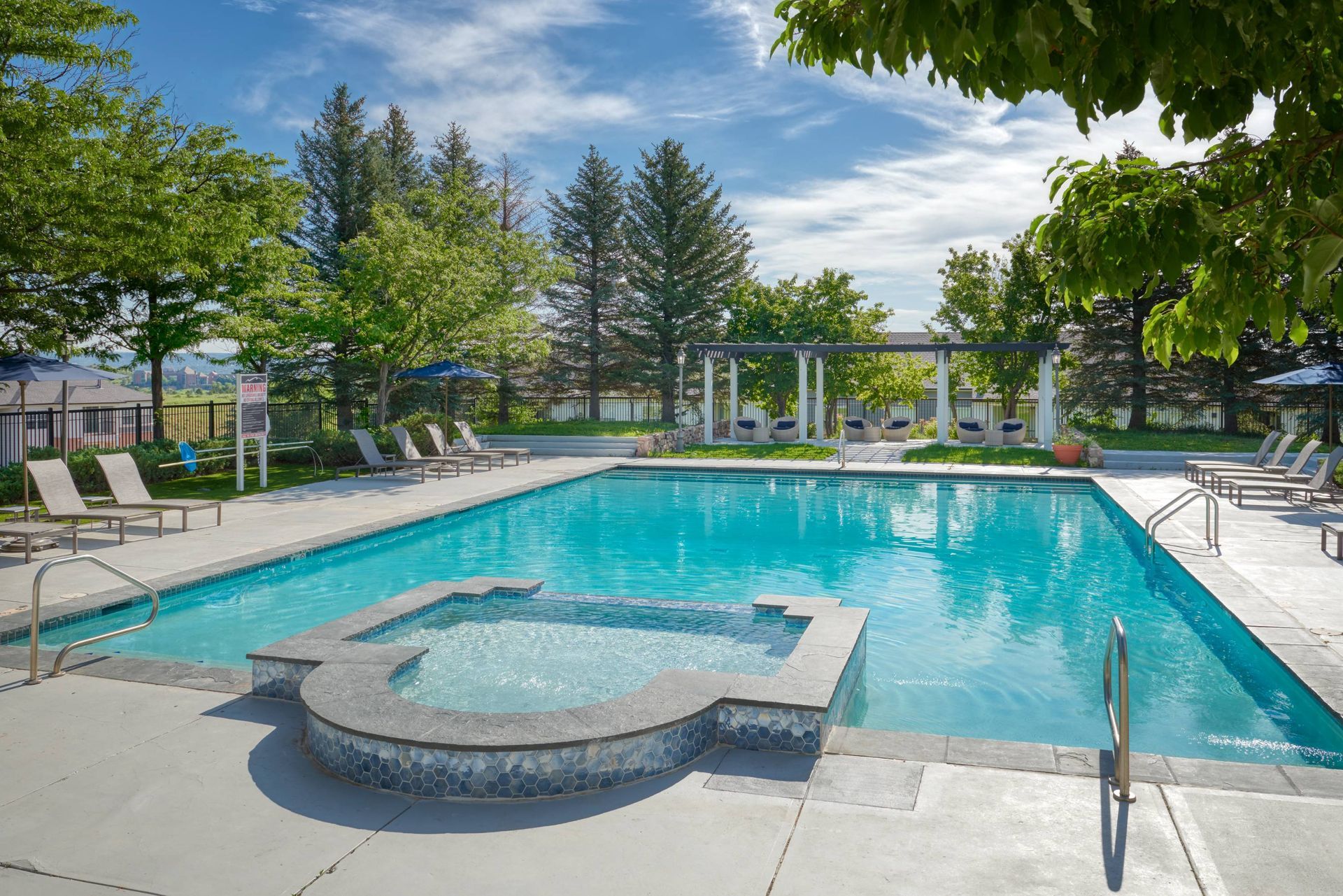 Outdoor community pool with lounge chairs and a shaded seating area under a pergola.