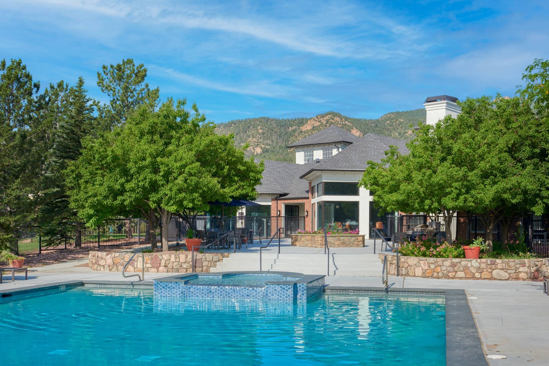 Outdoor apartment community pool with surrounding seating, trees, and mountain backdrop.