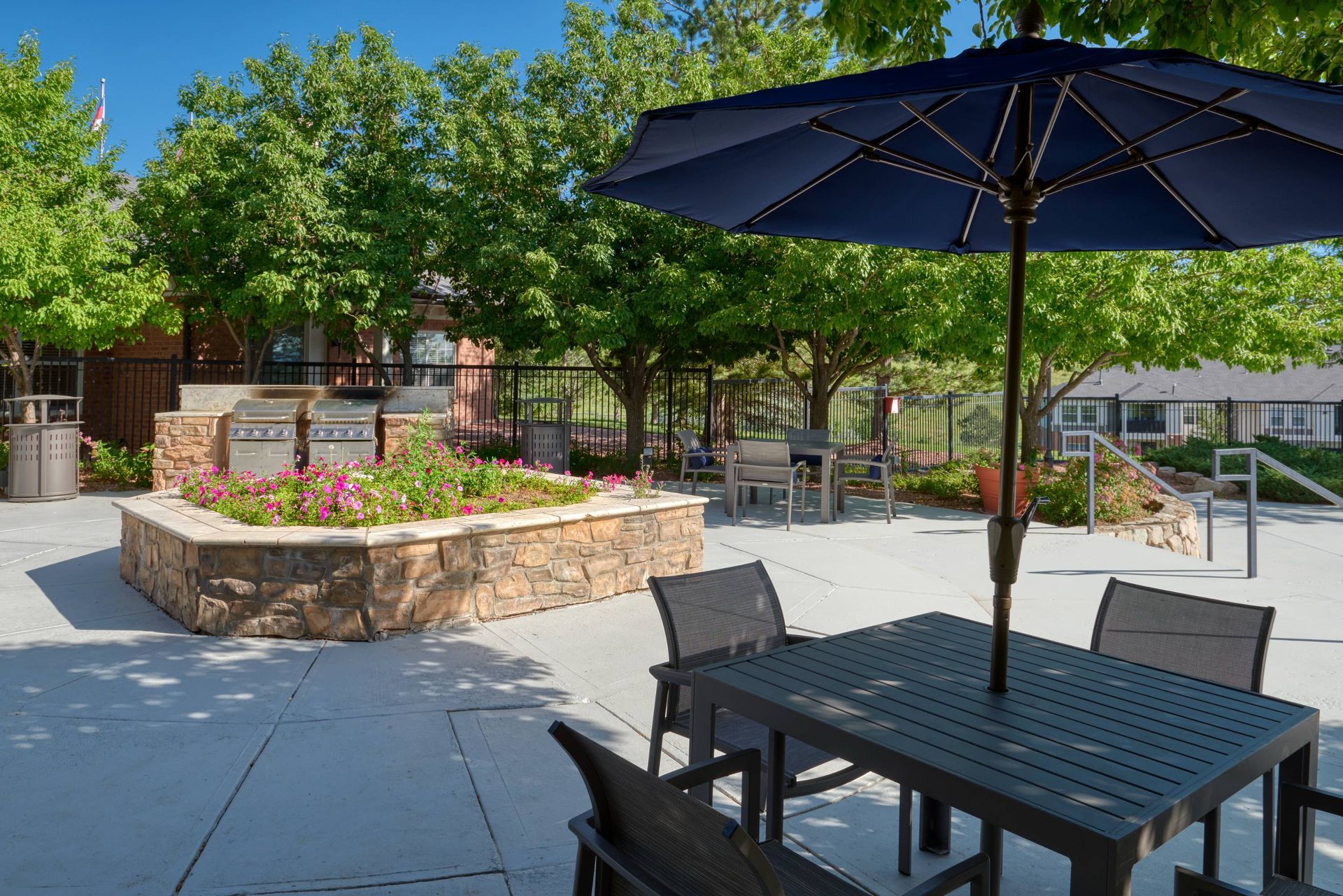 Outdoor communal courtyard with stone planter, grills, and seating under a large umbrella.