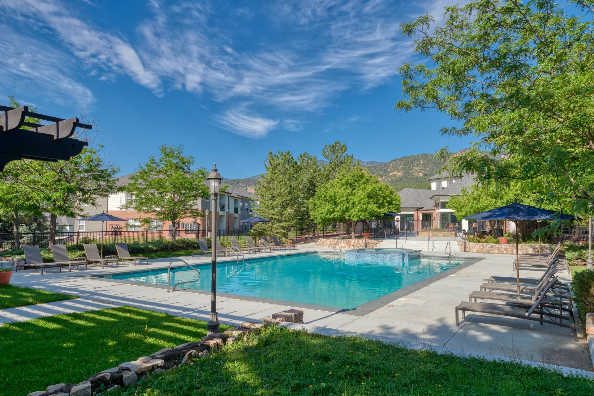 Outdoor apartment community pool with lounge chairs and umbrellas, set among trees with mountains in the background.