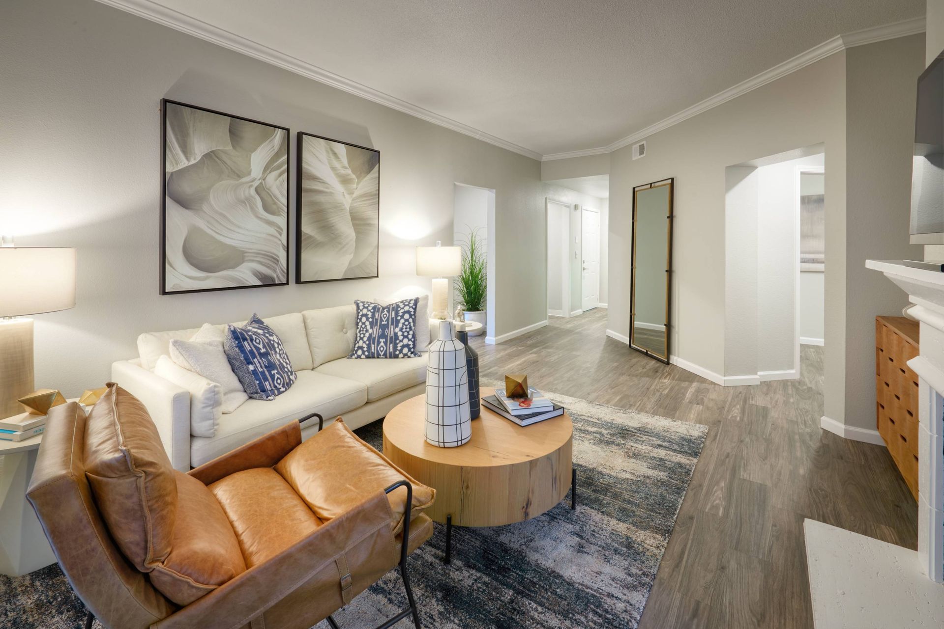 Bright living room featuring a white sofa, brown accent chair, round wooden coffee table, and wall art.