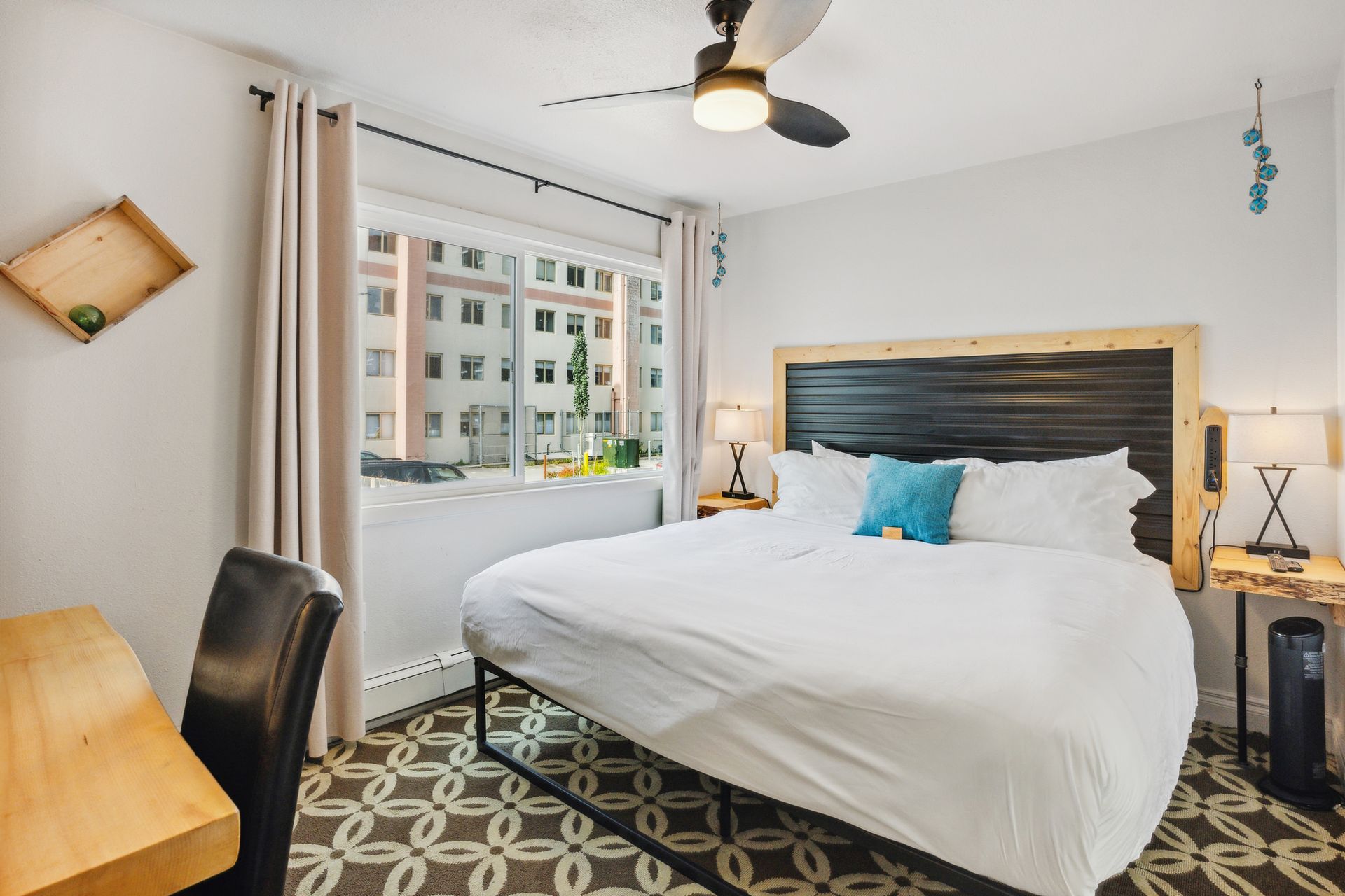 A hotel room with a king size bed , desk , chair and ceiling fan.