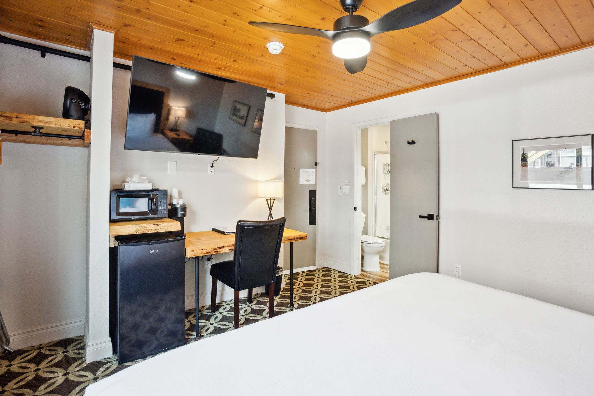 A hotel room with a bed , desk , chair , television and ceiling fan.