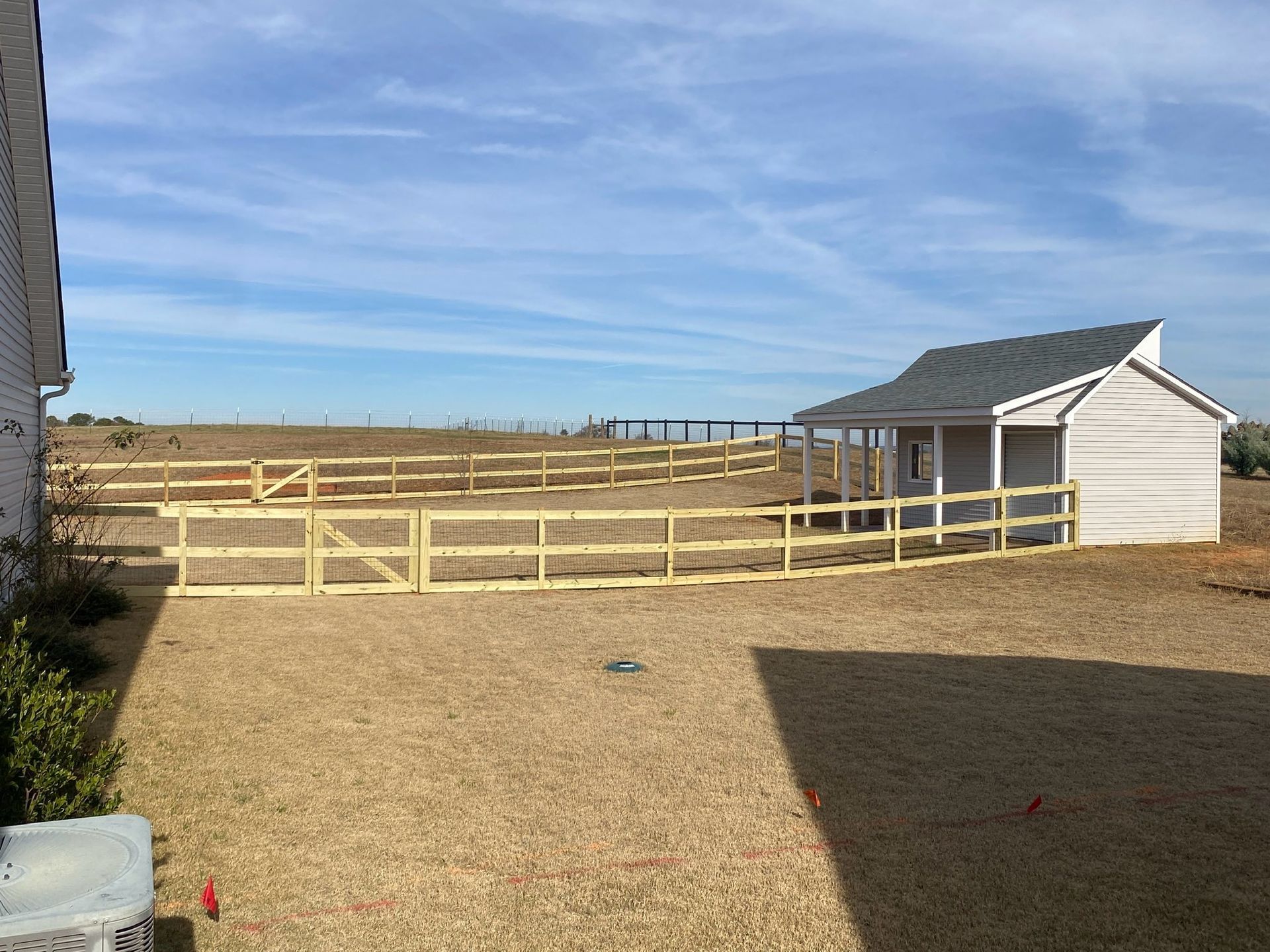 A wooden fence encloses a small pasture with a shed. The ground is dry grass, and the sky is blue.