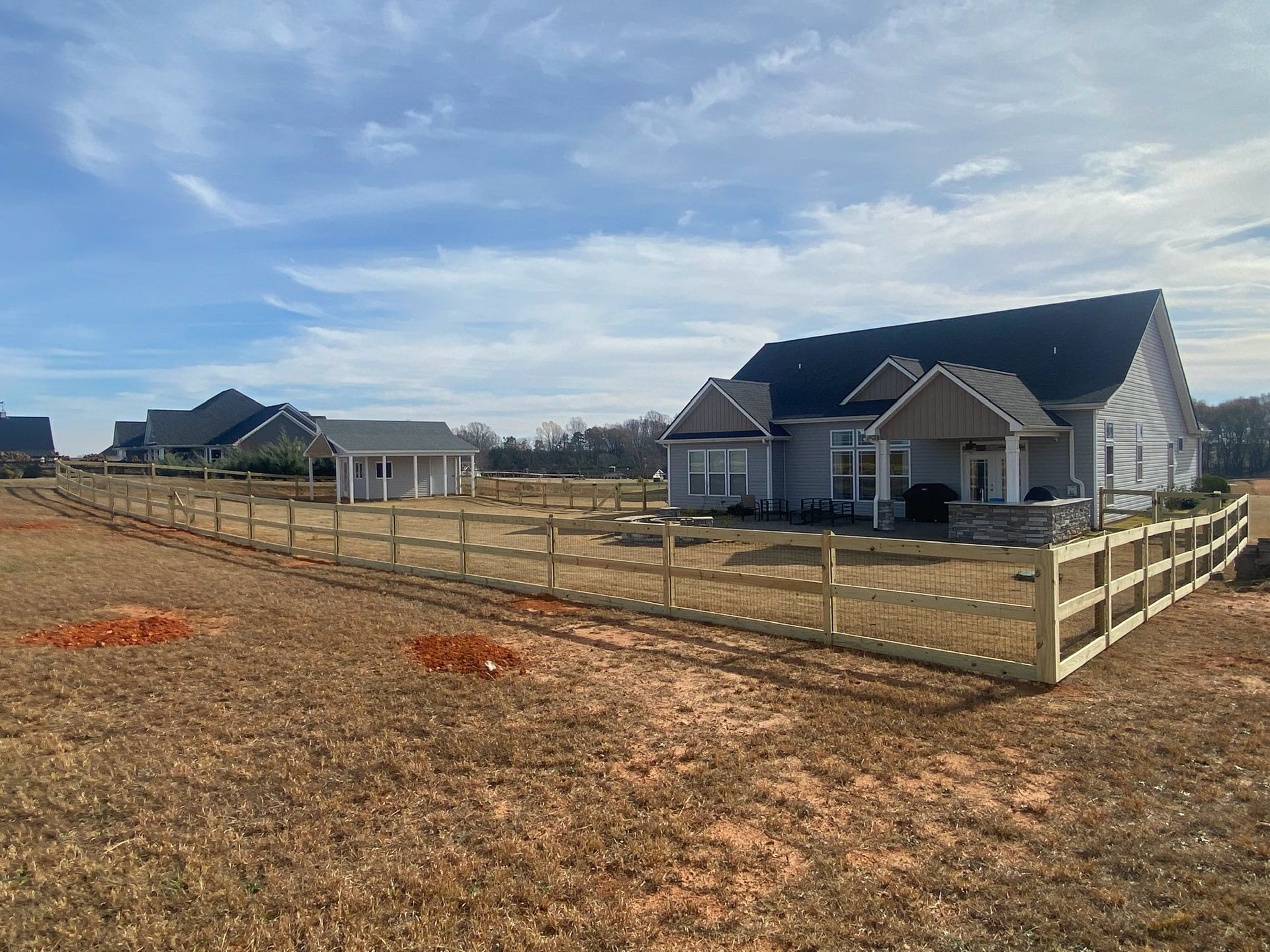 A newly built home with a wooden fence in a field, under a blue sky with sparse clouds.