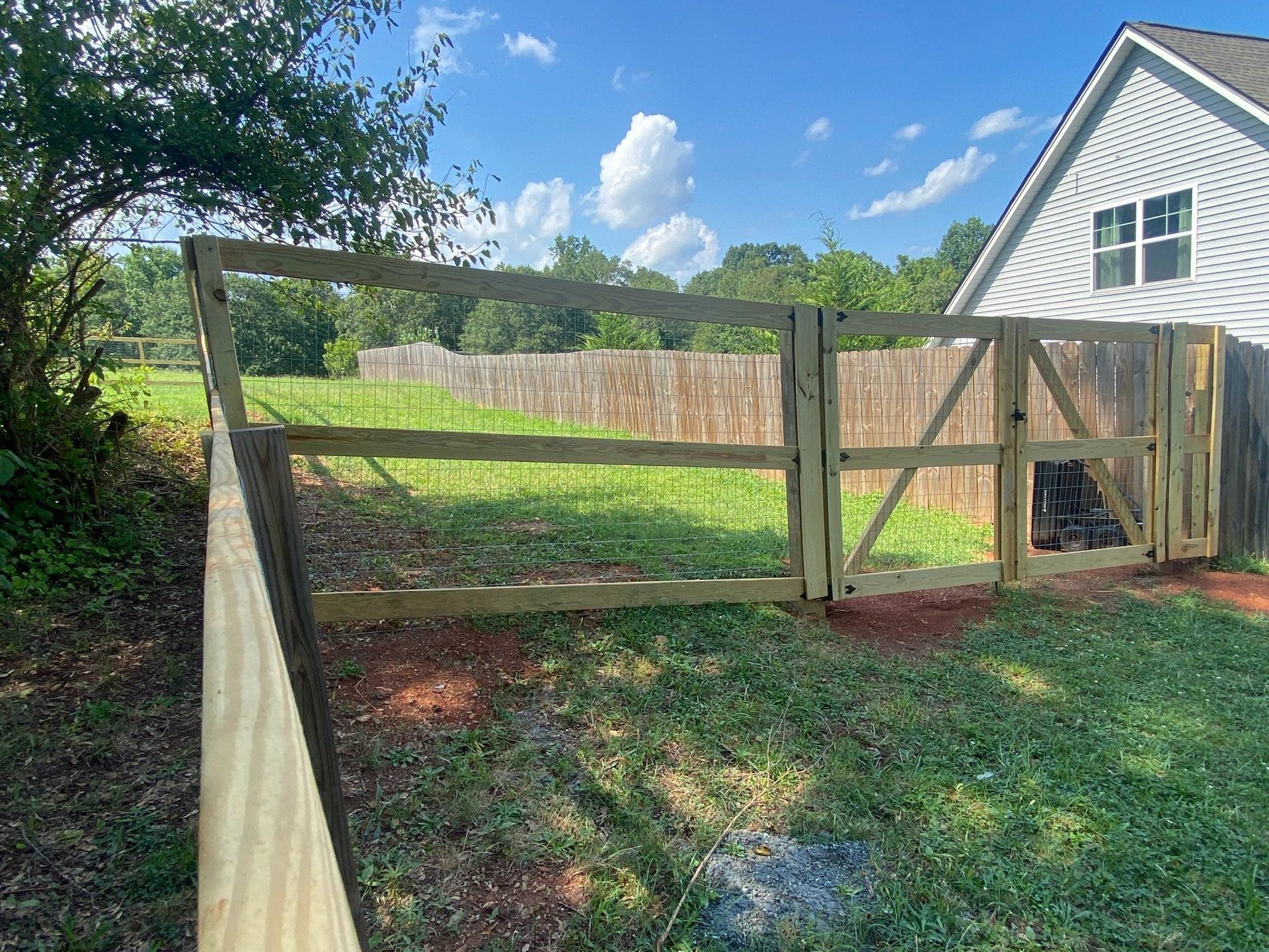 A newly constructed wooden fence and gate enclose a grassy backyard, under a partly cloudy sky.