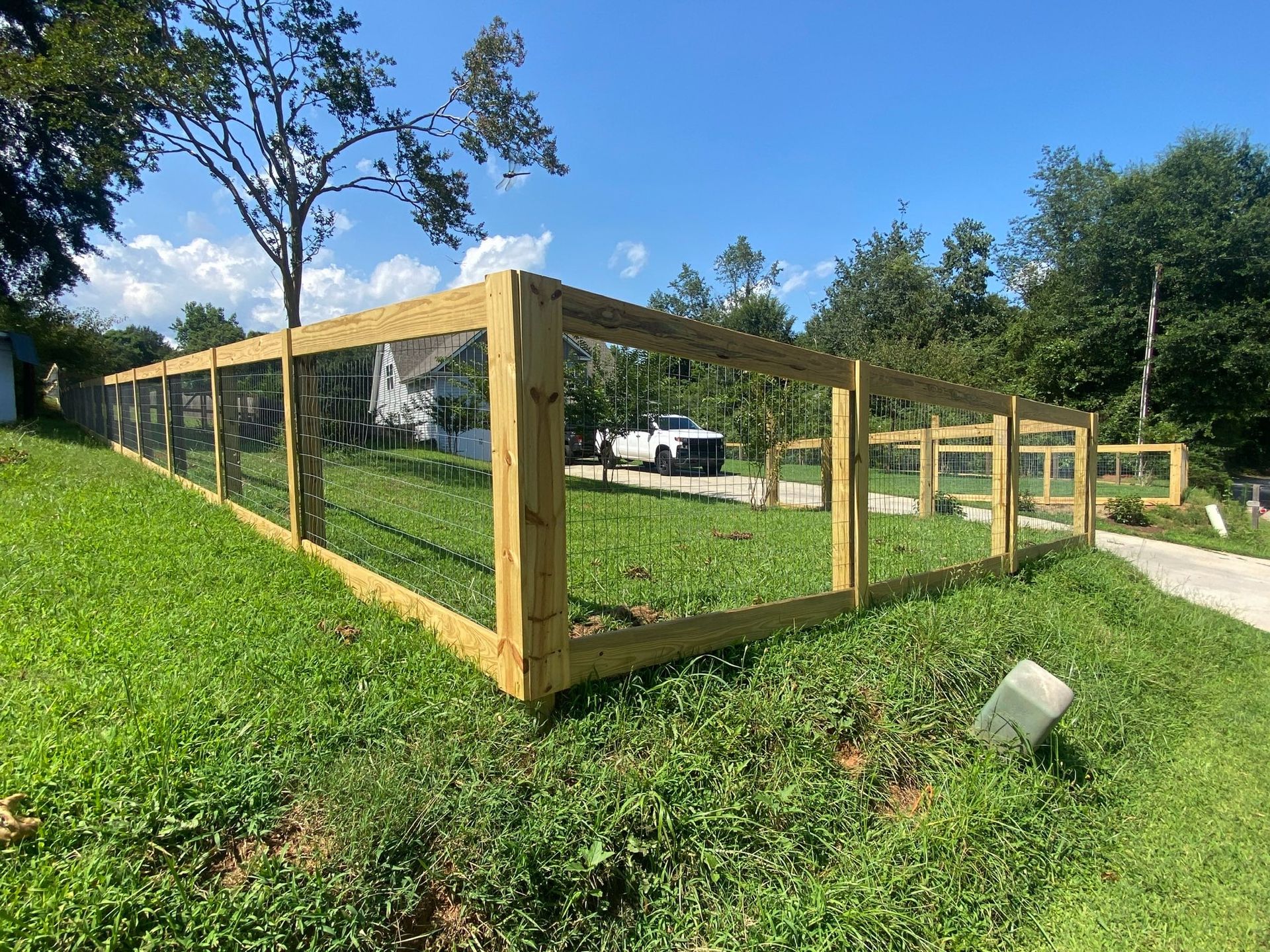 Newly built wooden fence with black mesh surrounds a grassy yard under a blue sky.