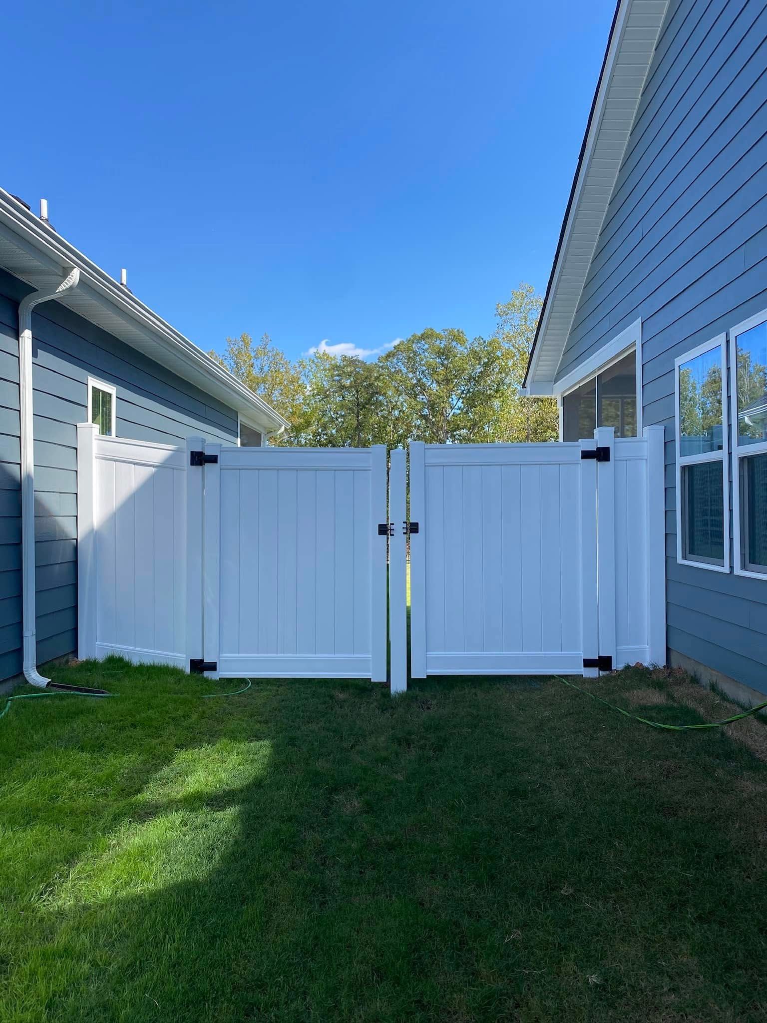 White double gate in a backyard, flanked by blue houses with green grass beneath a clear blue sky.