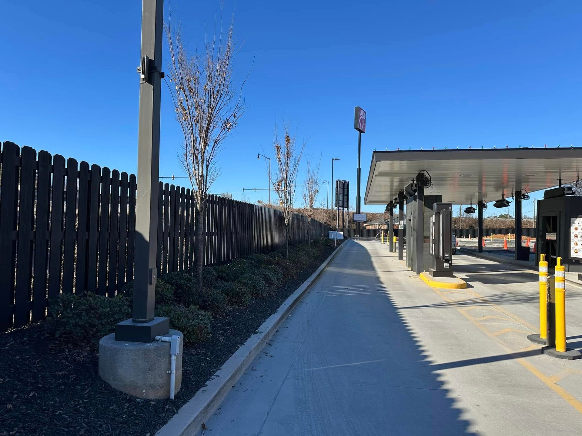 A drive-thru lane with a concrete path, fence, and canopy on a sunny day.