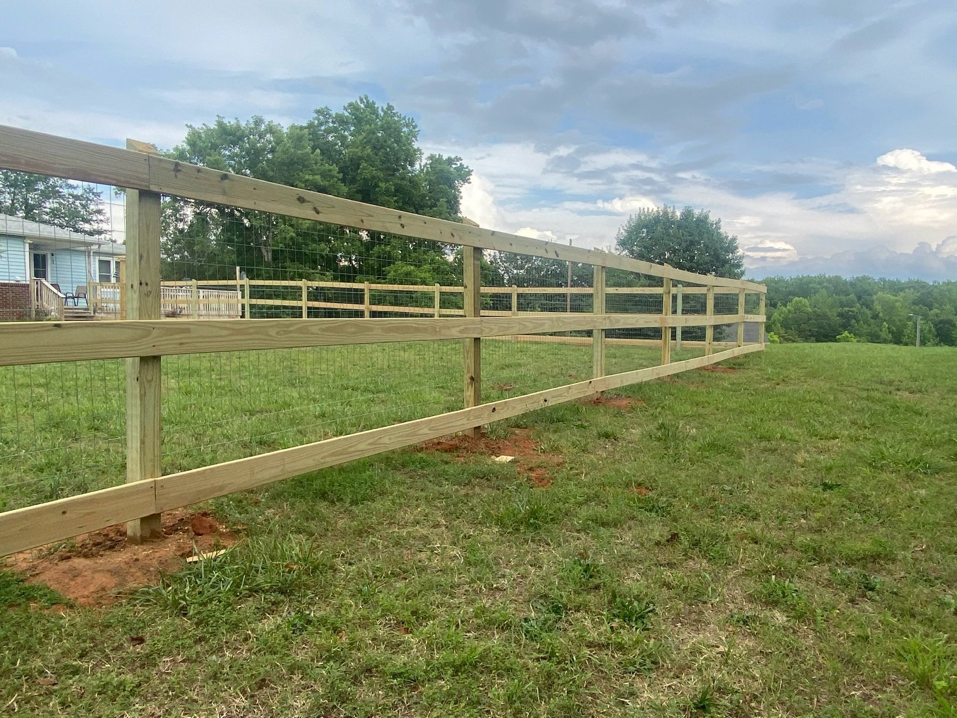 A newly built wooden fence in a grassy field under a cloudy sky.