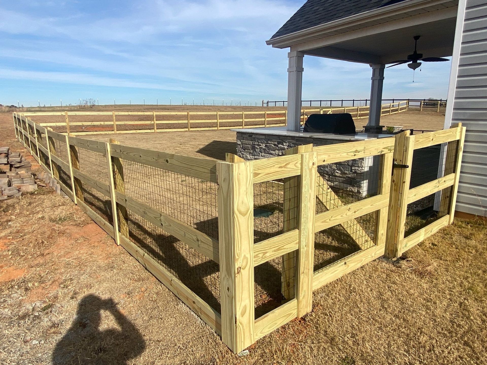 A newly built wooden fence surrounding a patio area, adjacent to a house under a clear blue sky.