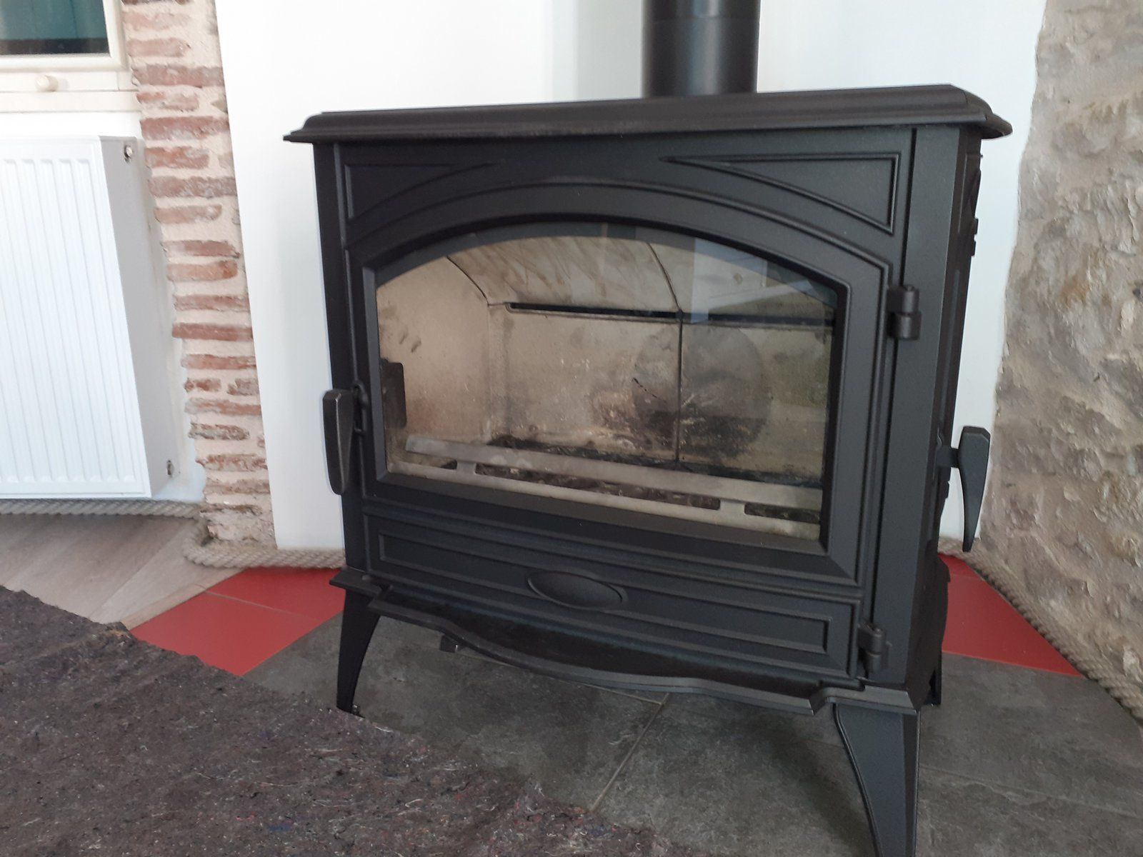 Poêle de cheminée en fonte noire avec porte vitrée, installé sur un foyer adossé à un mur en pierre.