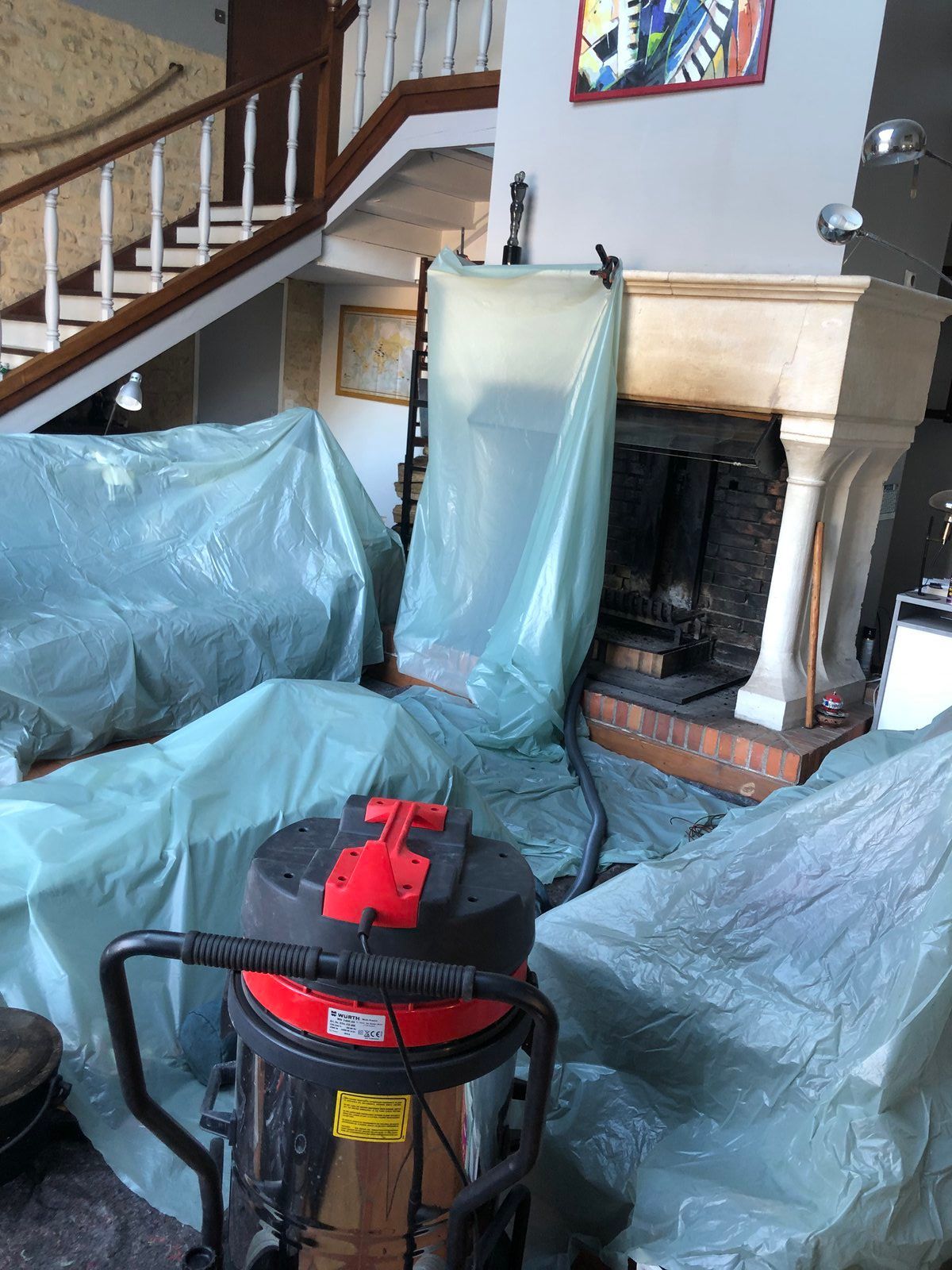 Salon avec des meubles recouverts de plastique bleu et un aspirateur rouge et noir au premier plan