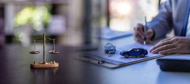 An auto accident attorney signing documents with a car model, keys, and a justice scale on his desk.