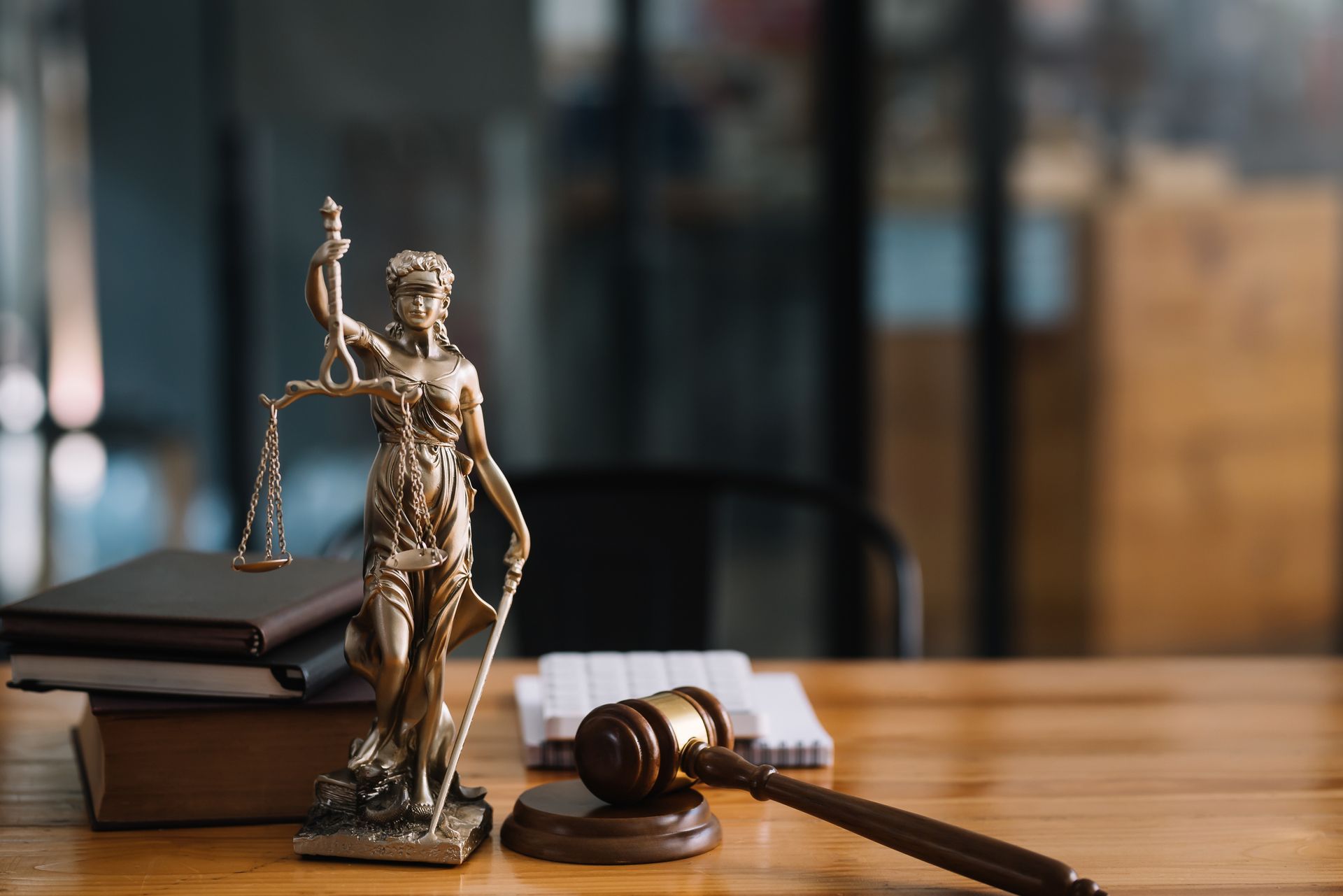 Statue of Lady Justice with scales, gavel, and books on a wooden table, symbolizing law and justice.