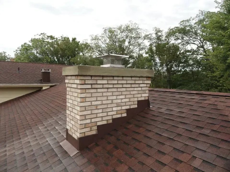 A brick chimney on top of a roof with trees in the background