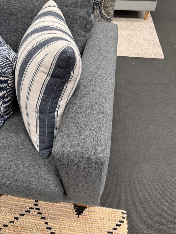 Close-up of a gray sofa arm with a striped pillow and a patterned rug in the foreground.