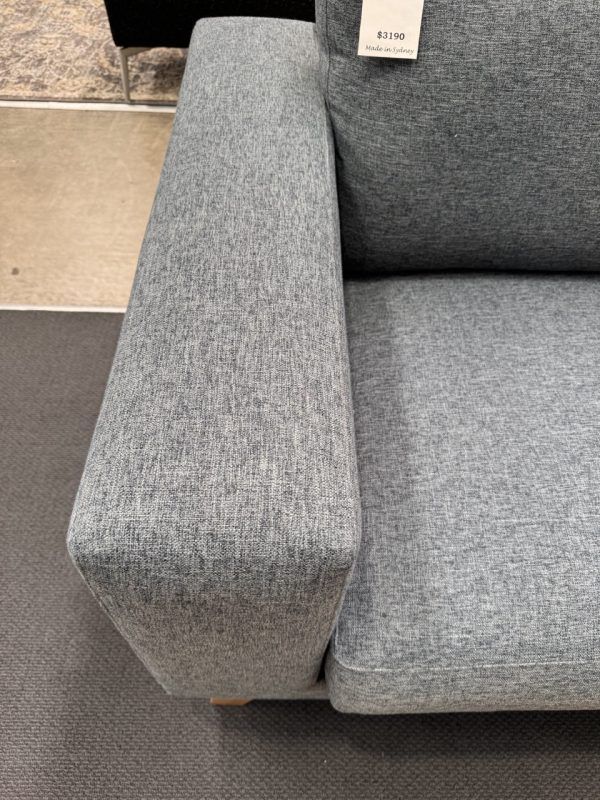 Close-up of a gray sofa arm and cushion. The fabric has a textured look, and a price tag is visible.