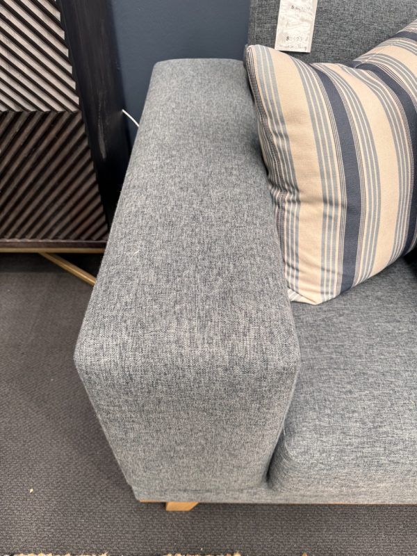 Close-up of a gray upholstered sofa arm with a striped pillow, indoors.
