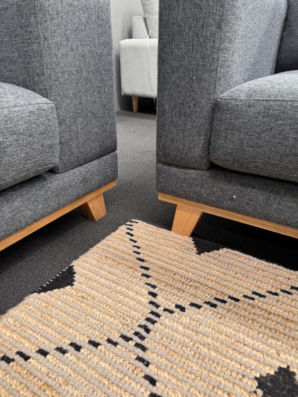 Two gray armchairs on wooden legs, beside a patterned rug, in a room.