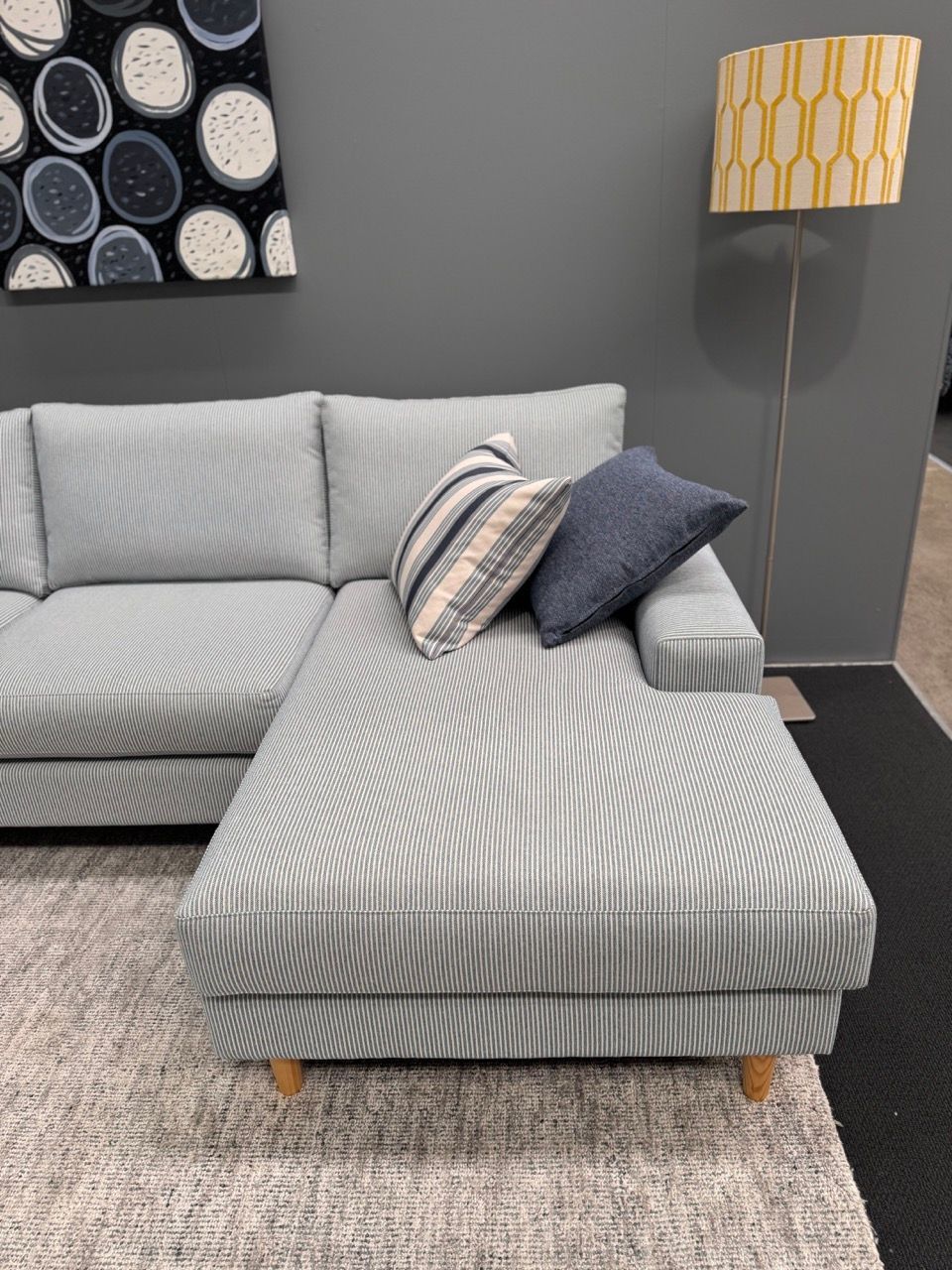 Light blue sectional sofa with patterned fabric and pillows. Gray wall, floor lamp, and rug.