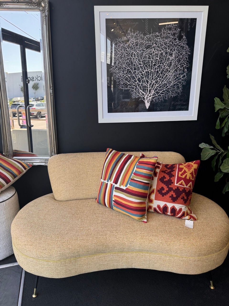 Curved beige sofa with colorful pillows against black wall, framed art, and mirror.