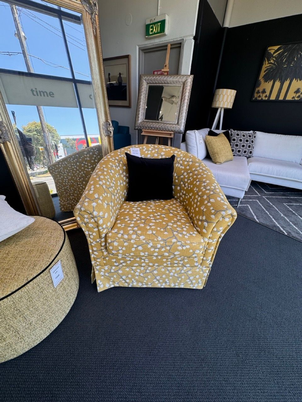 Yellow patterned armchair with a black pillow in a store setting.