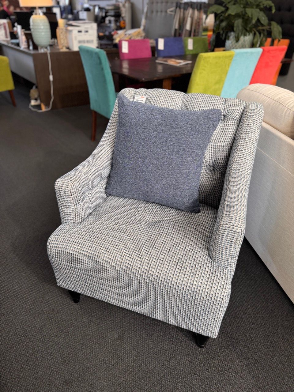 Upholstered armchair with blue and white pattern and a blue pillow, in a showroom.