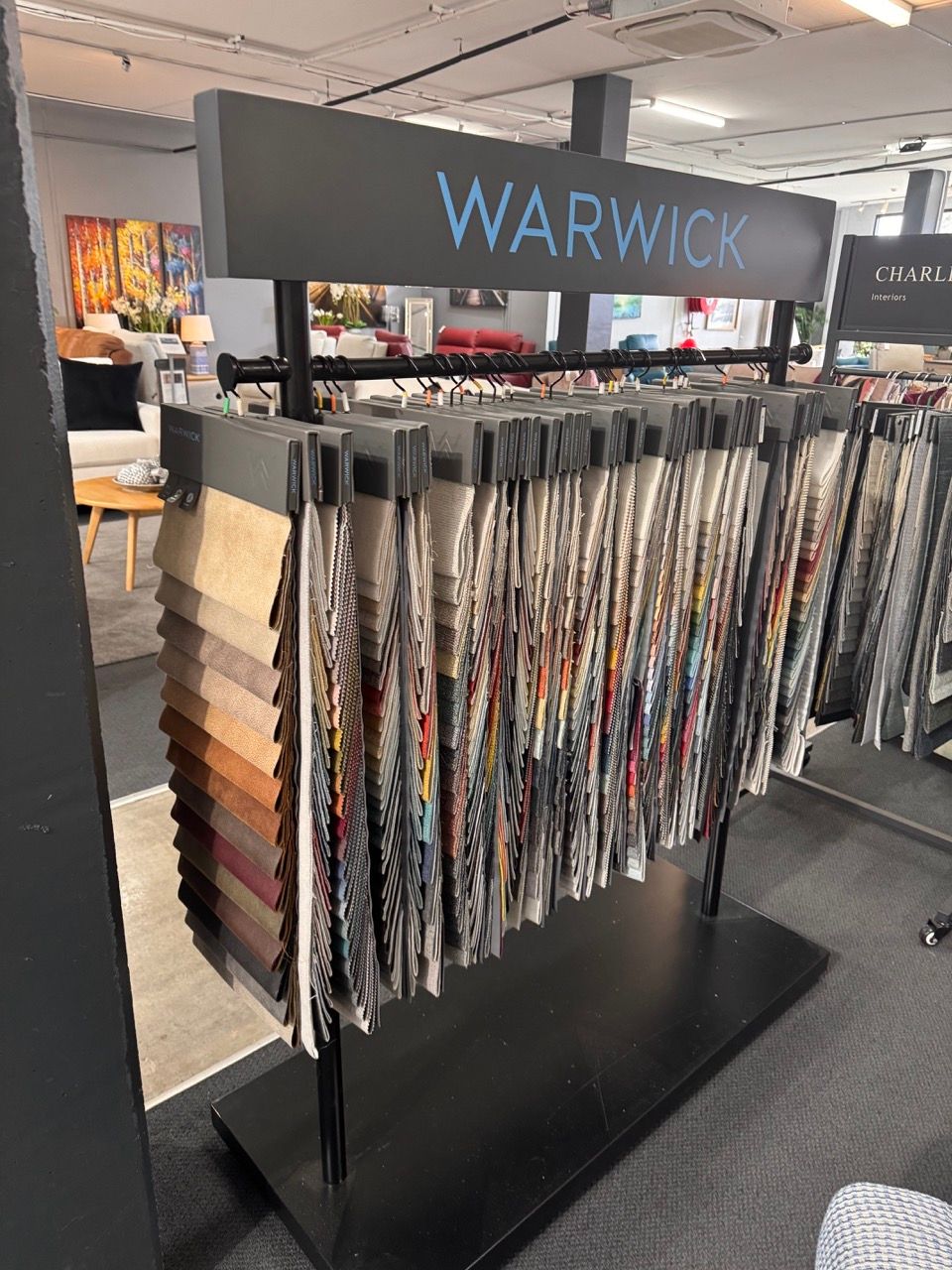 Fabric samples displayed on a Warwick branded rack in a store. Variety of colors and patterns.
