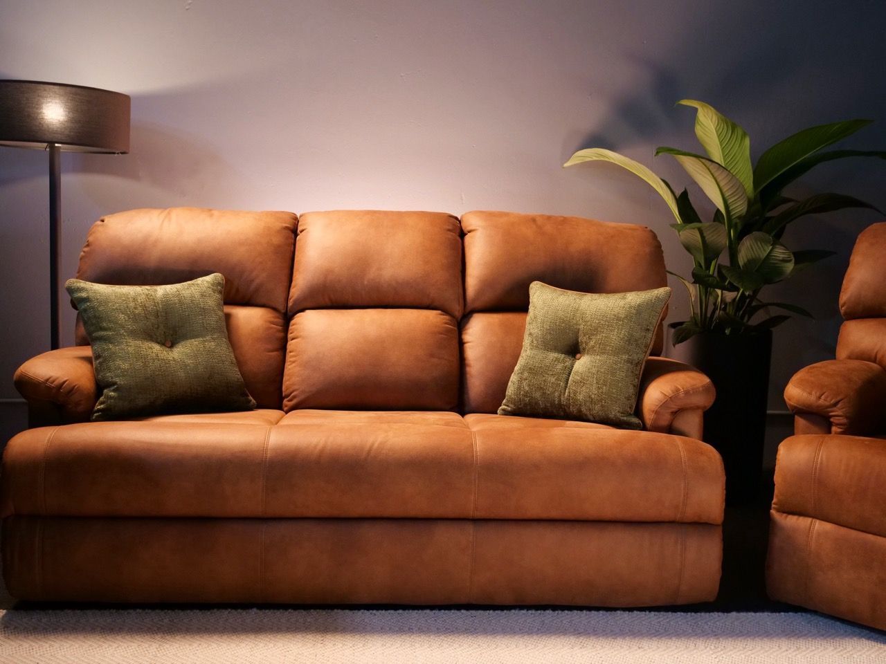 Brown leather sofa with green throw pillows, next to a houseplant and lamp.