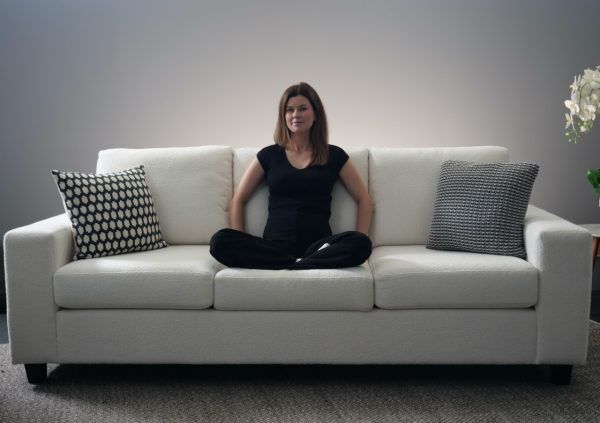 Woman seated on a white couch in a meditative pose, wearing black clothing. Decorative pillows.