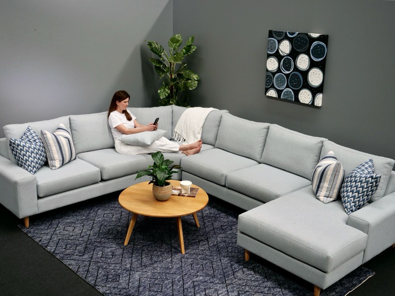 Woman on a gray sectional sofa, using her phone. Wooden coffee table, abstract art, indoor setting.