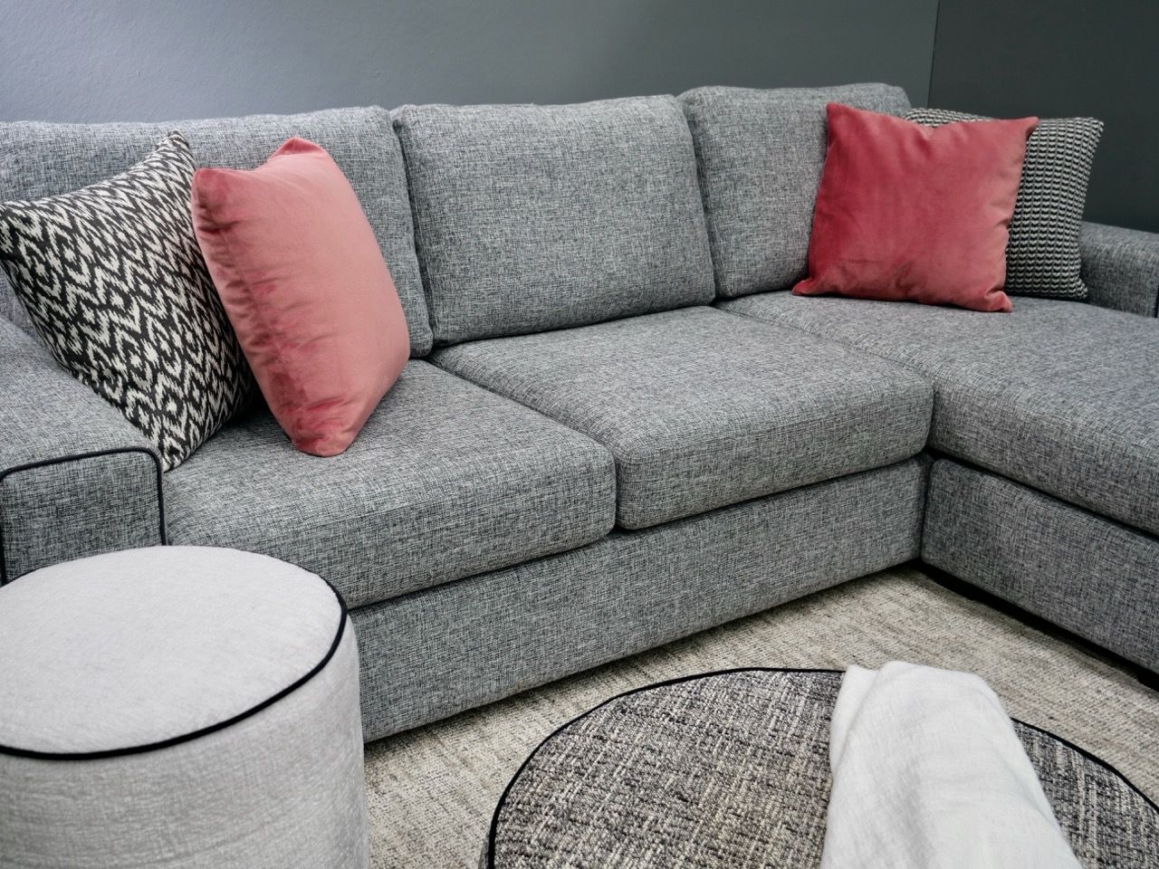 Gray sectional sofa with pink and patterned pillows, round ottoman, and round rug.