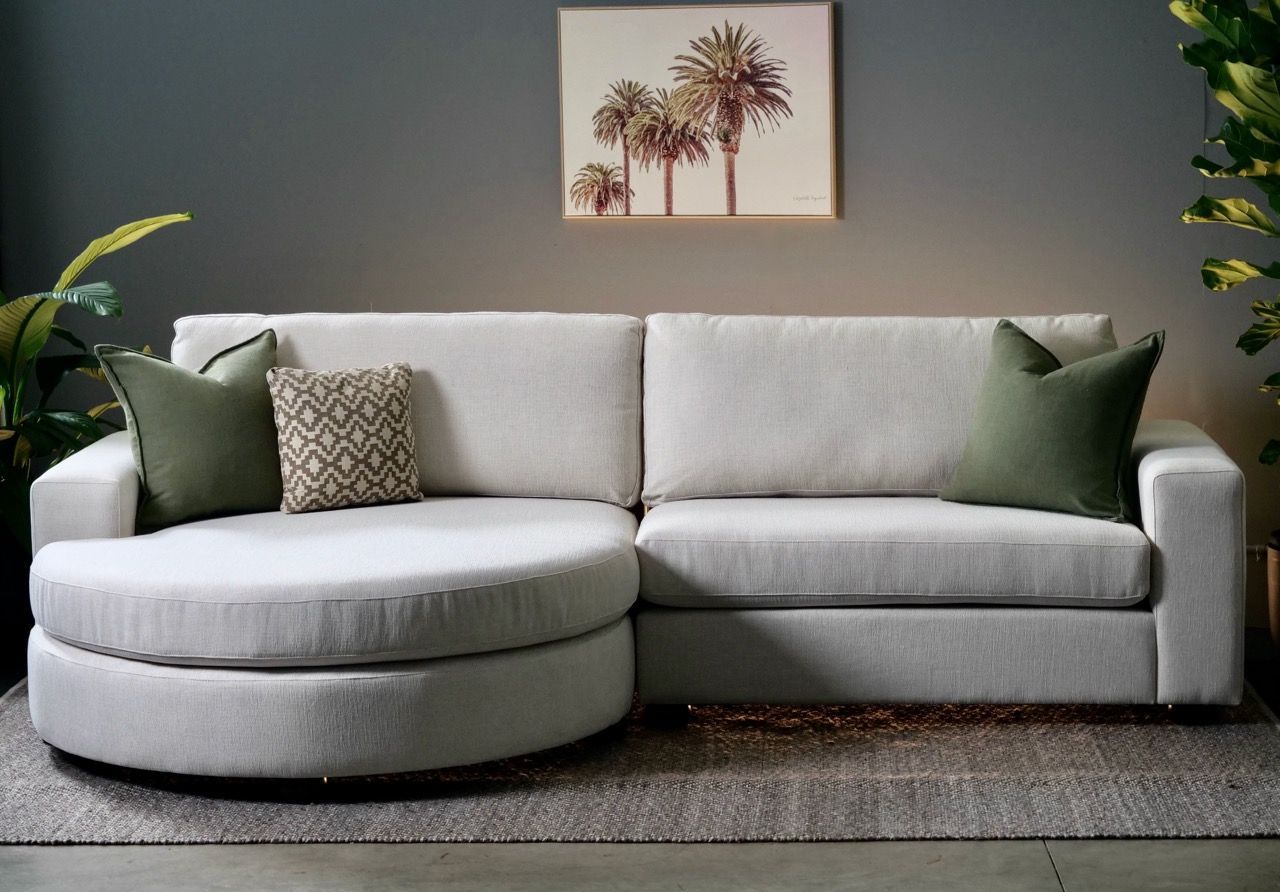 White sectional sofa with a round chaise and green pillows in a modern living room.