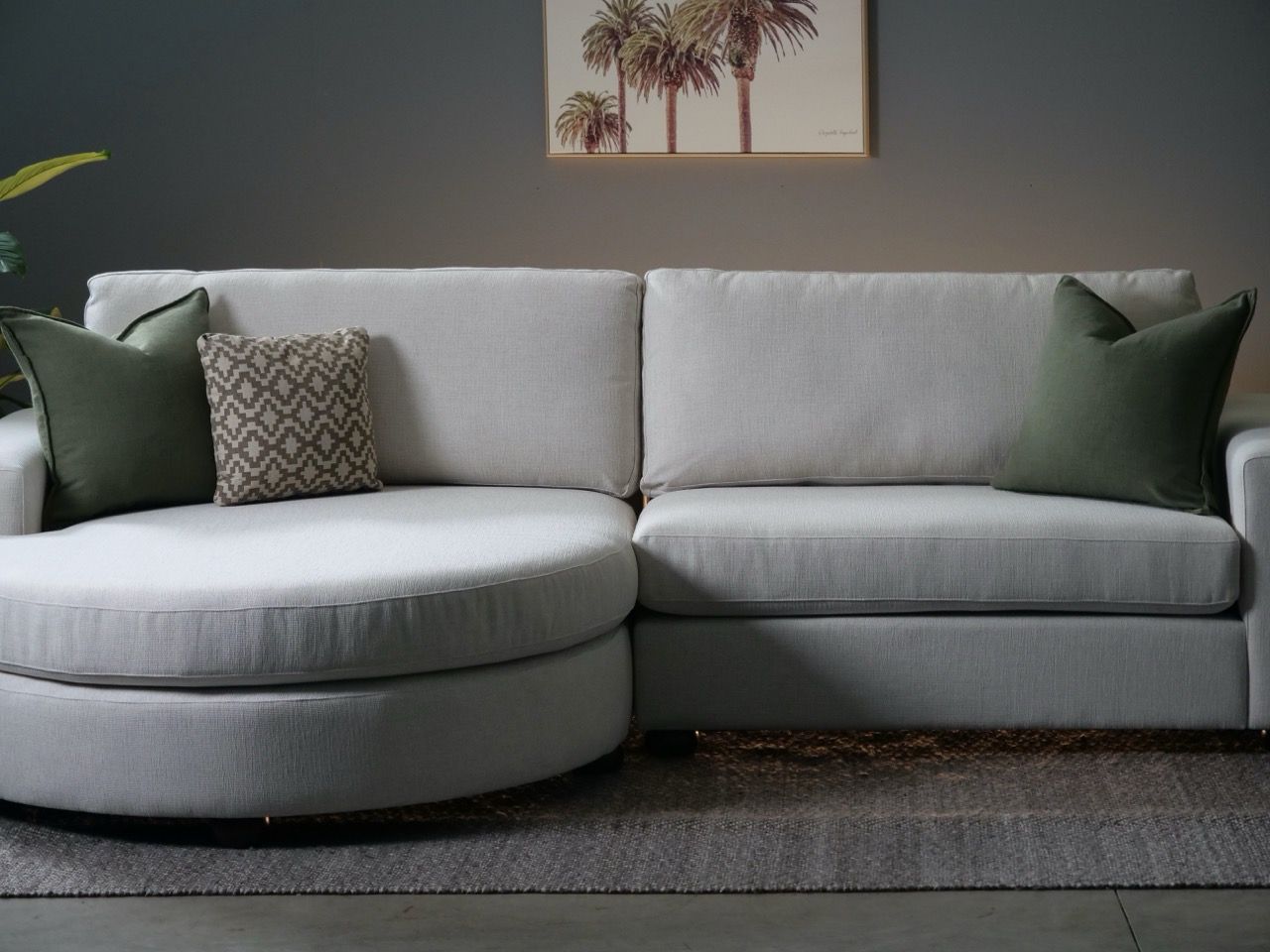 Light gray sectional sofa with round chaise, two green and one patterned pillow.