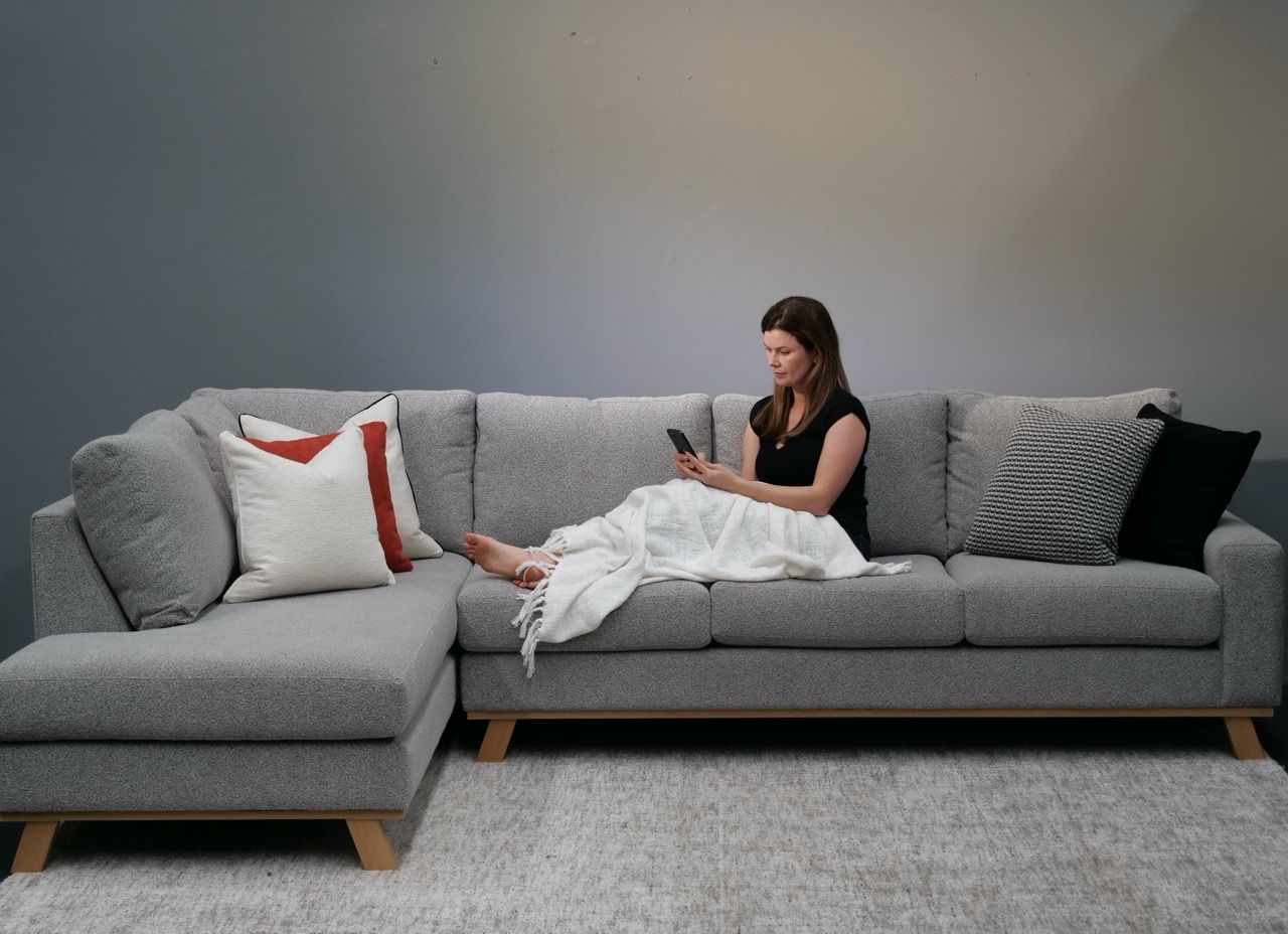 Woman sitting on gray sectional sofa, looking at phone.