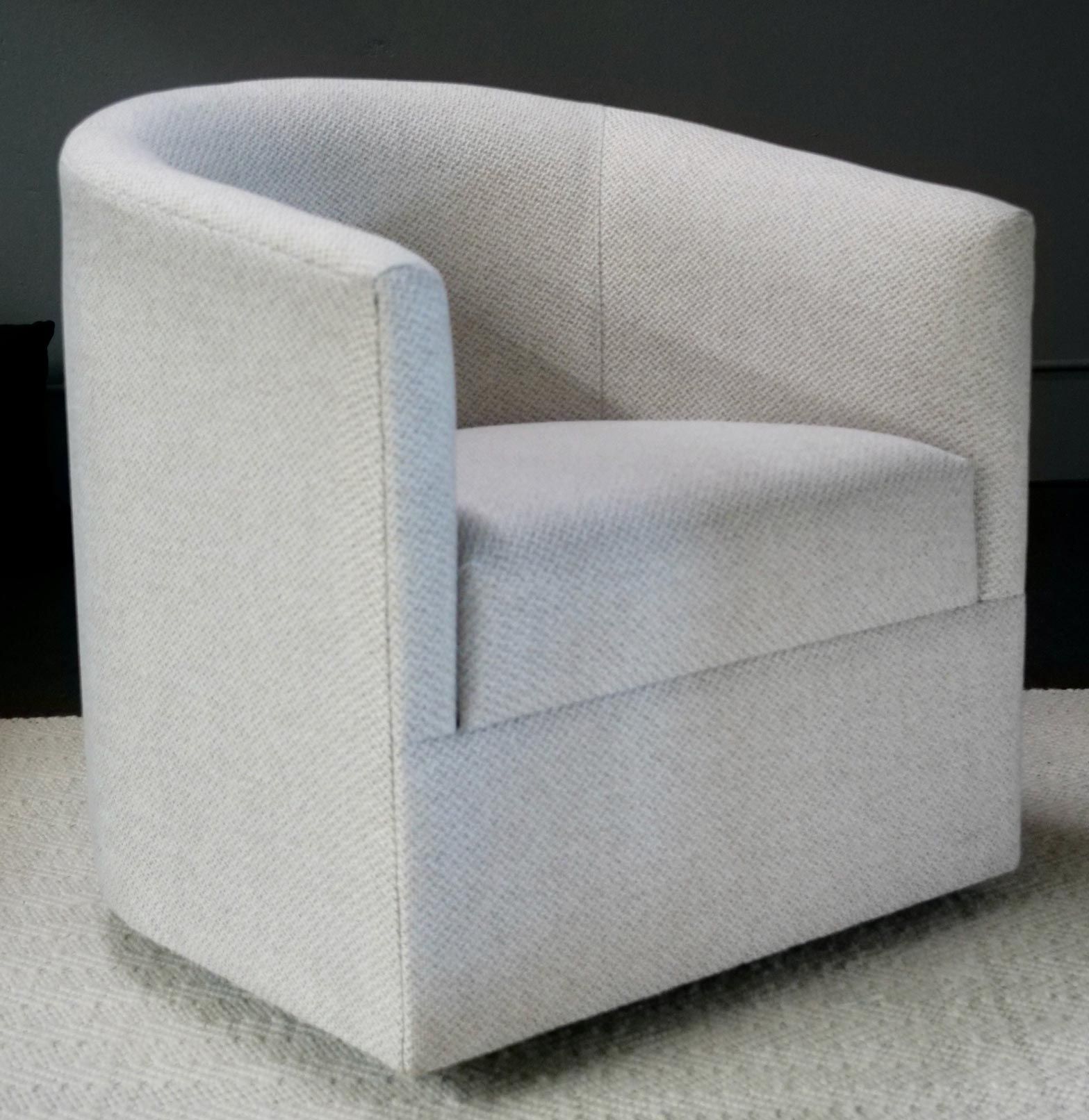 Cream-colored, upholstered barrel chair on a light rug, with a rounded back and square seat.